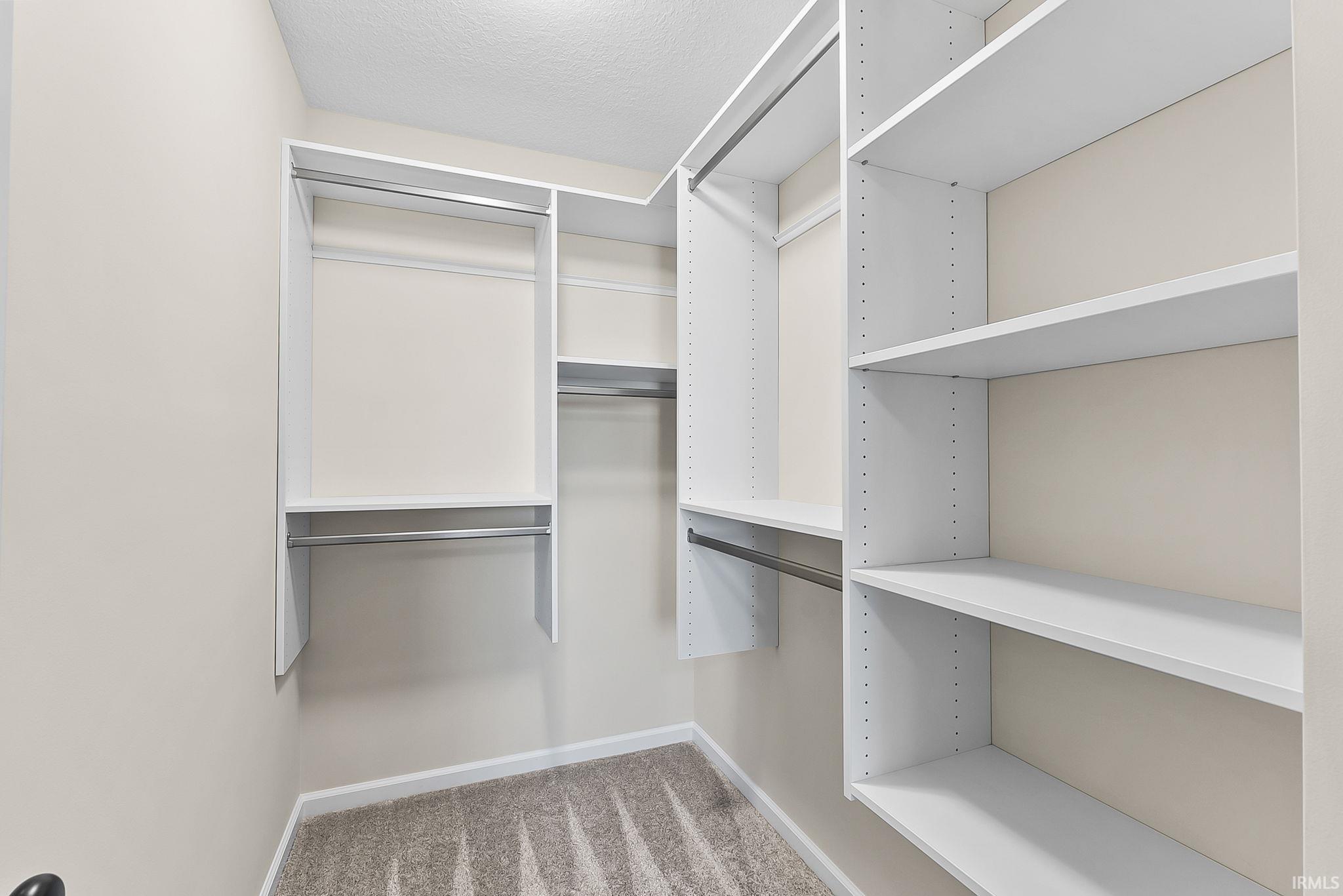 Walk-in closet featuring built-in white shelving, multiple hanging rods, neutral wall paint, and patterned carpet flooring