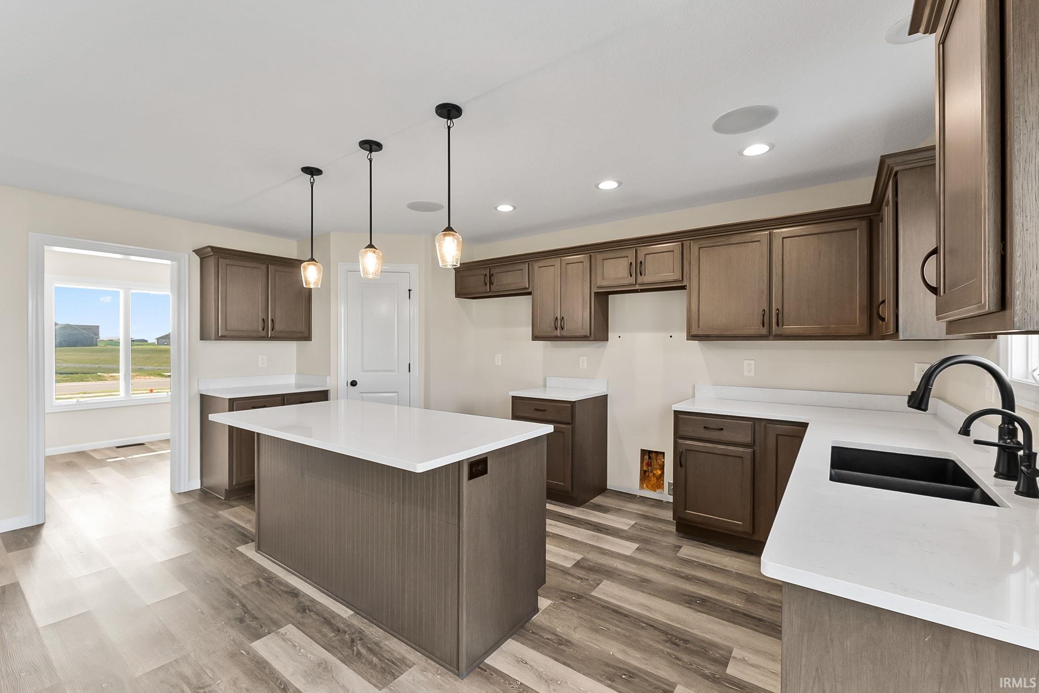 Spacious kitchen featuring an island with three pendant lights, wood-finish flooring, white countertops, and dark wood cabinetry