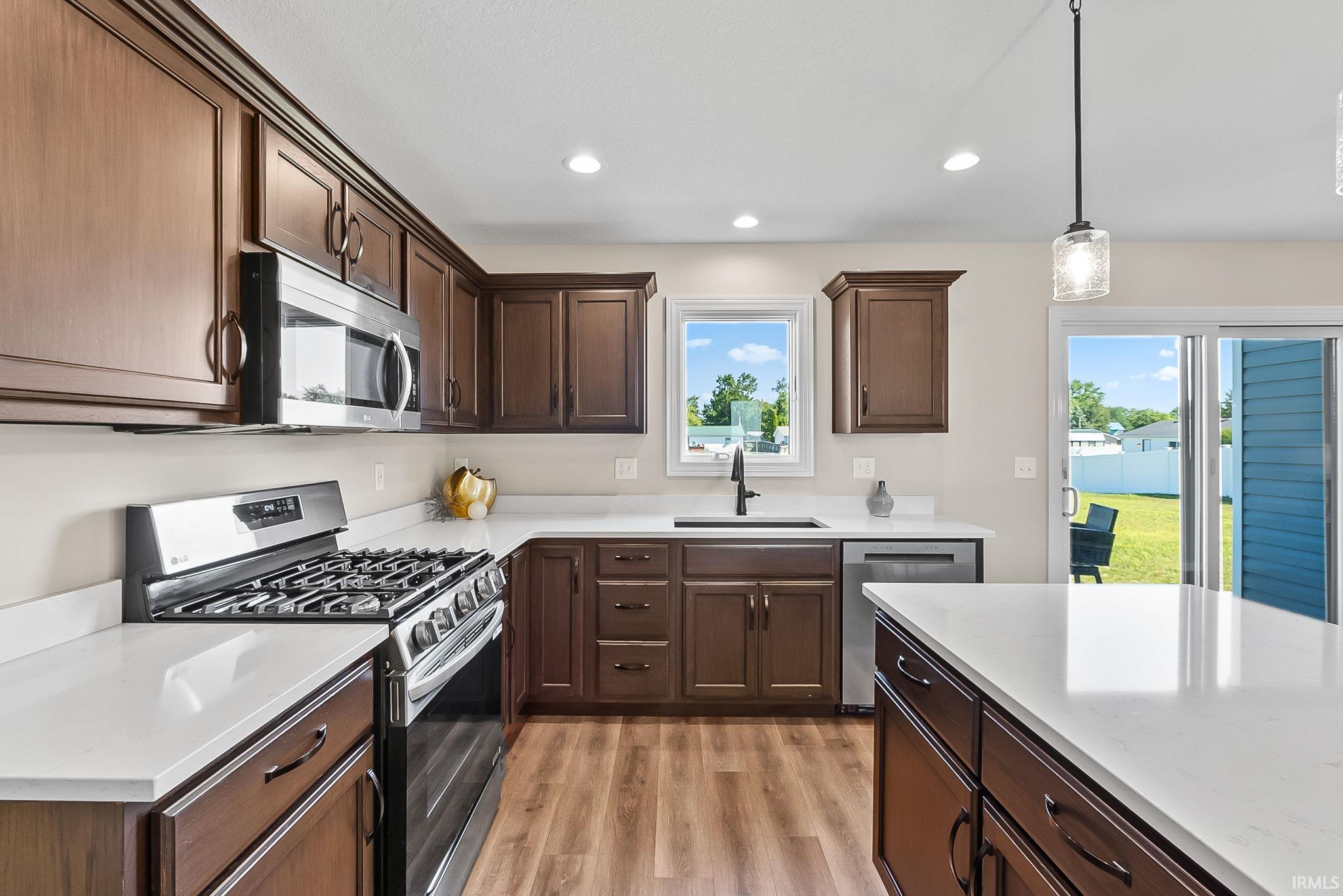 Kitchen featuring wood-finish flooring, dark wood cabinetry, white countertops, and stainless steel appliances