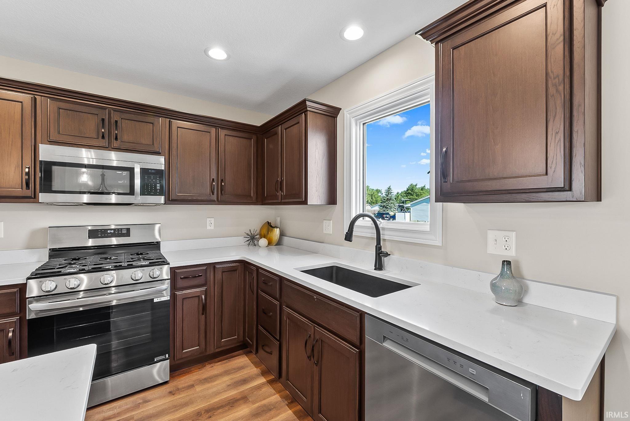 Contemporary kitchen featuring rich wood-finish cabinetry, stainless steel gas range with overhead microwave, and dual undermount sinks with matte black faucets