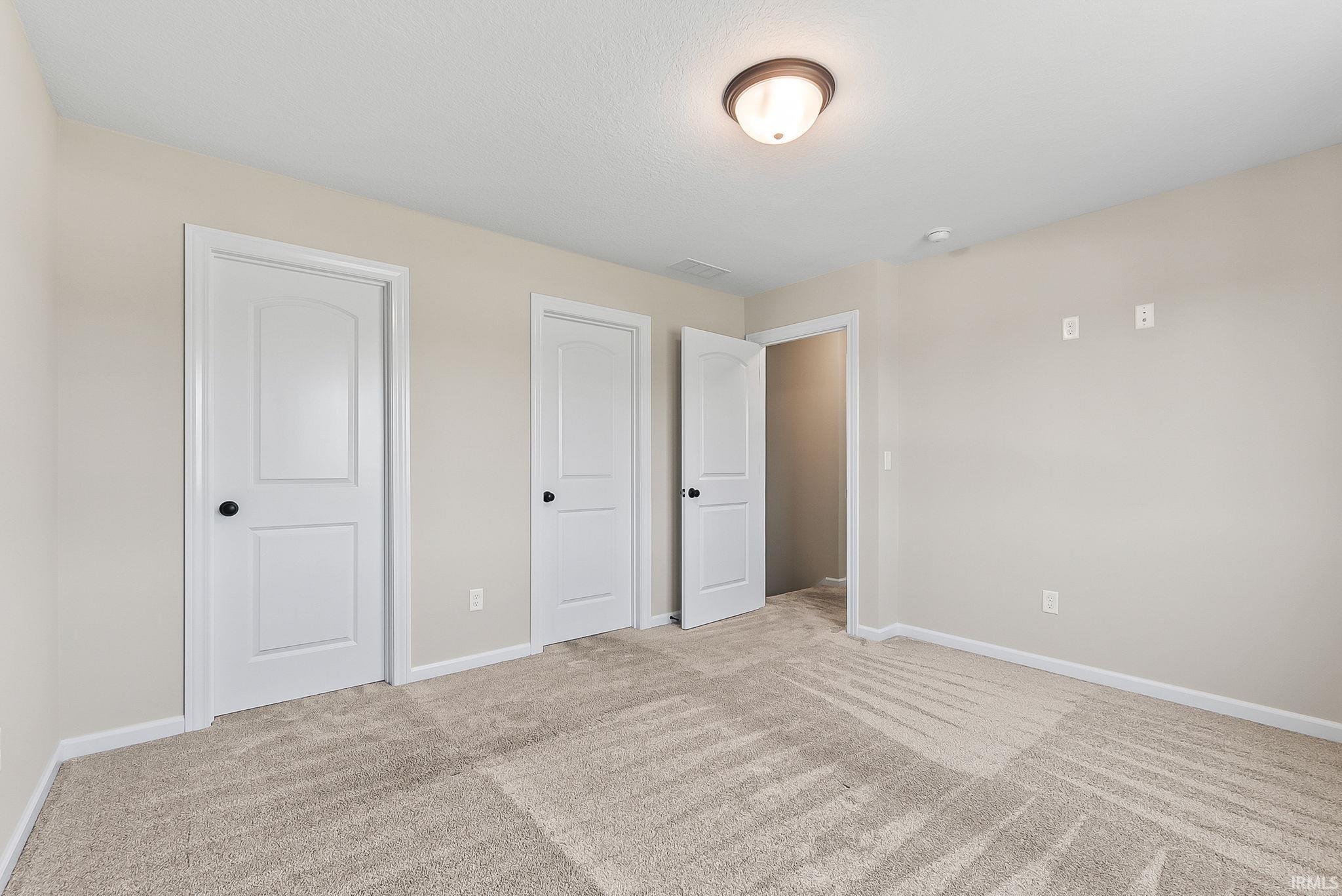 Neutral-toned room featuring a single semi-flush mount ceiling light, light beige carpeting, white baseboards, and multiple white paneled doors with matte black hardware