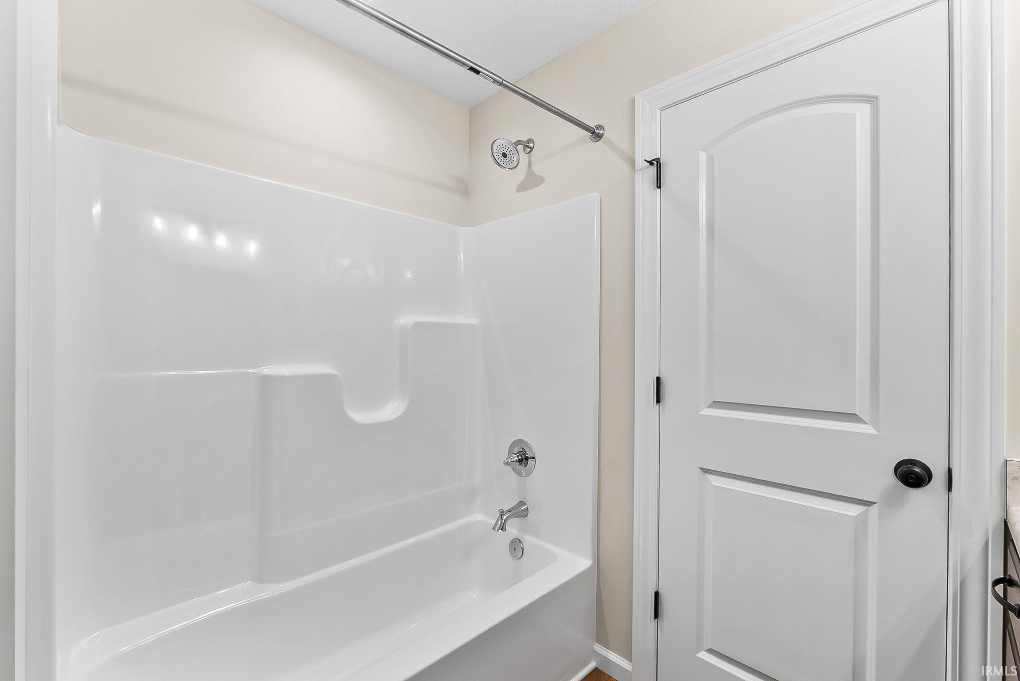 Clean and functional bathroom featuring a white tile shower surround with built-in shelving, chrome fixtures, and a soaking tub