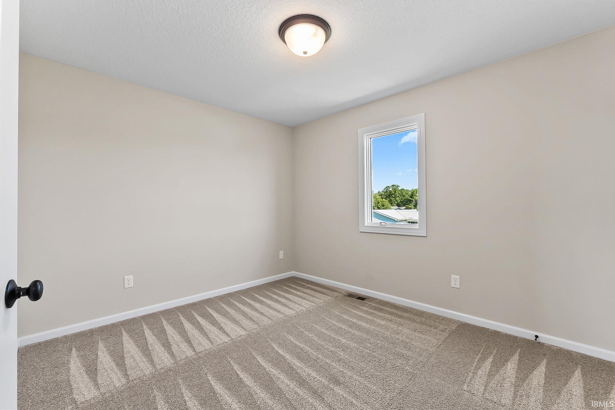 Neutral-toned interior with light tan walls, a single window, and textured carpet flooring