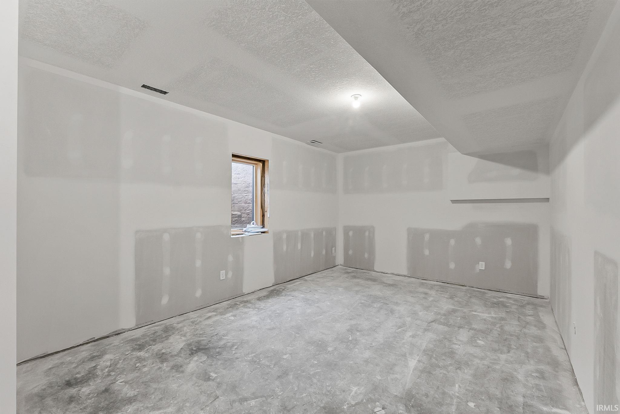 Spacious interior room featuring fresh drywall installation, concrete flooring, recessed ceiling lighting, and a single opaque window