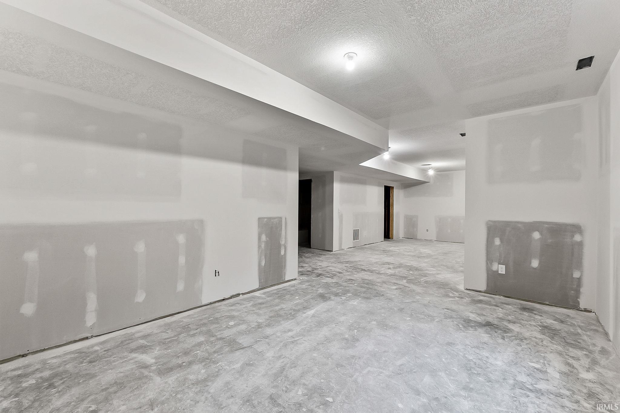 Unfinished basement with exposed concrete flooring, drywall-ready walls, and multiple ceiling light fixtures