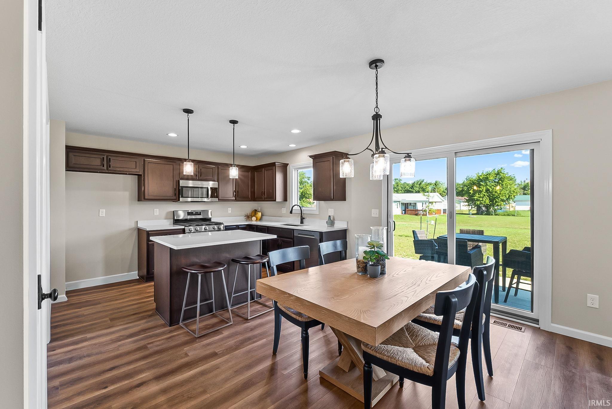 Open-concept kitchen and dining area featuring wood-finish flooring, dark wood cabinetry, white countertops, and stainless steel appliances