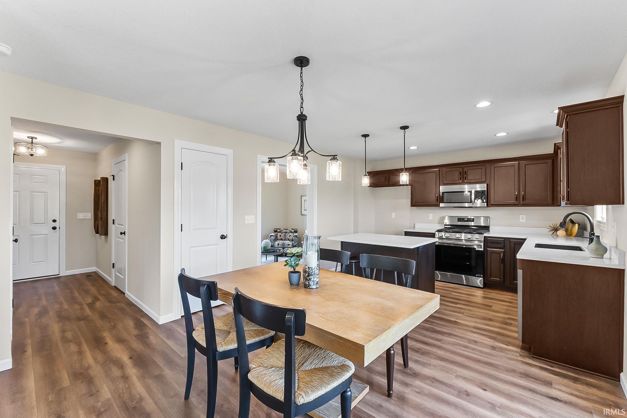 Kitchen and dining area featuring wood-finish flooring, dark wood cabinetry, stainless steel appliances, and white countertops