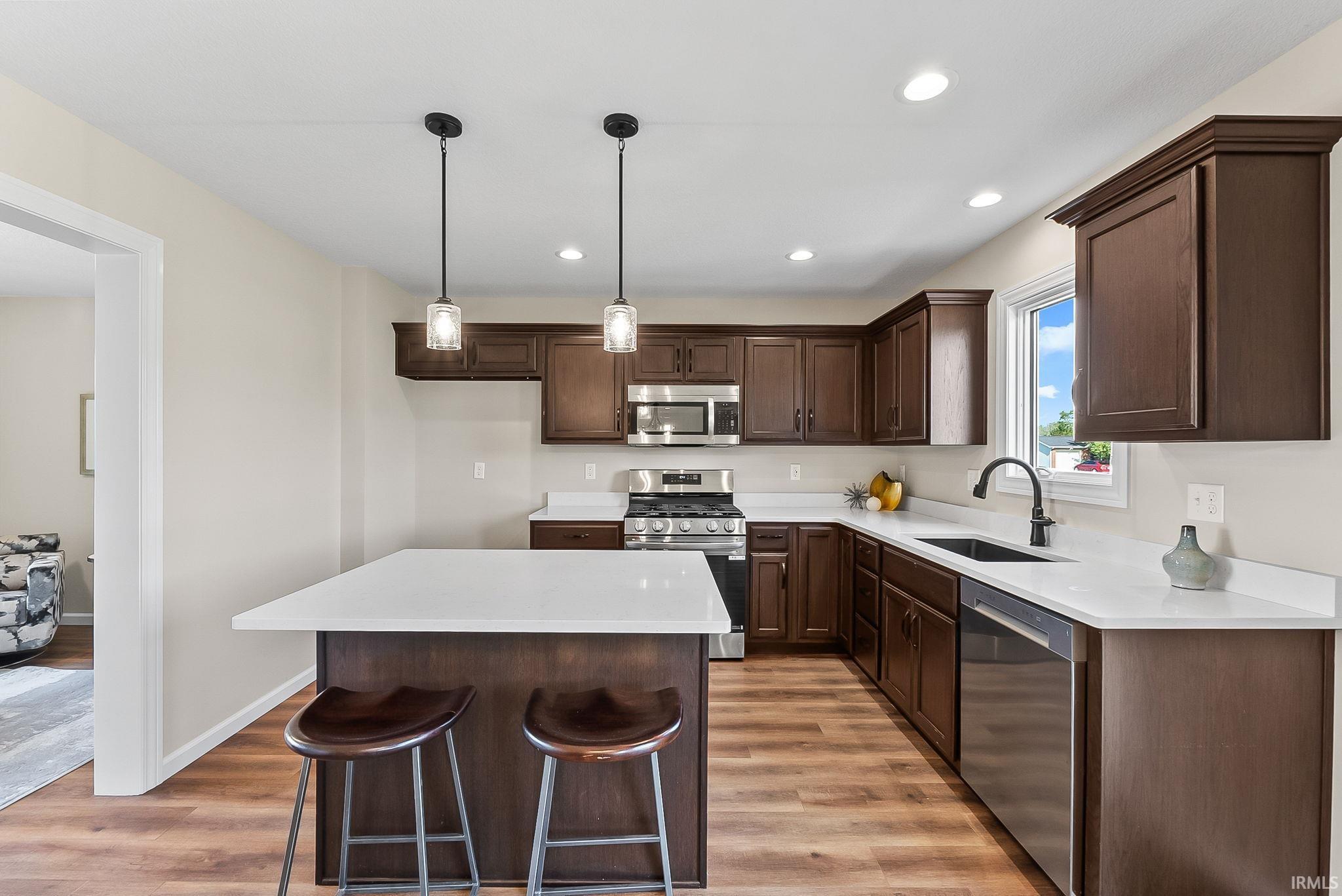 Modern kitchen featuring rich cabinetry, stainless steel appliances, a center island with pendant lighting, solid surface countertops, and wood-finish flooring
