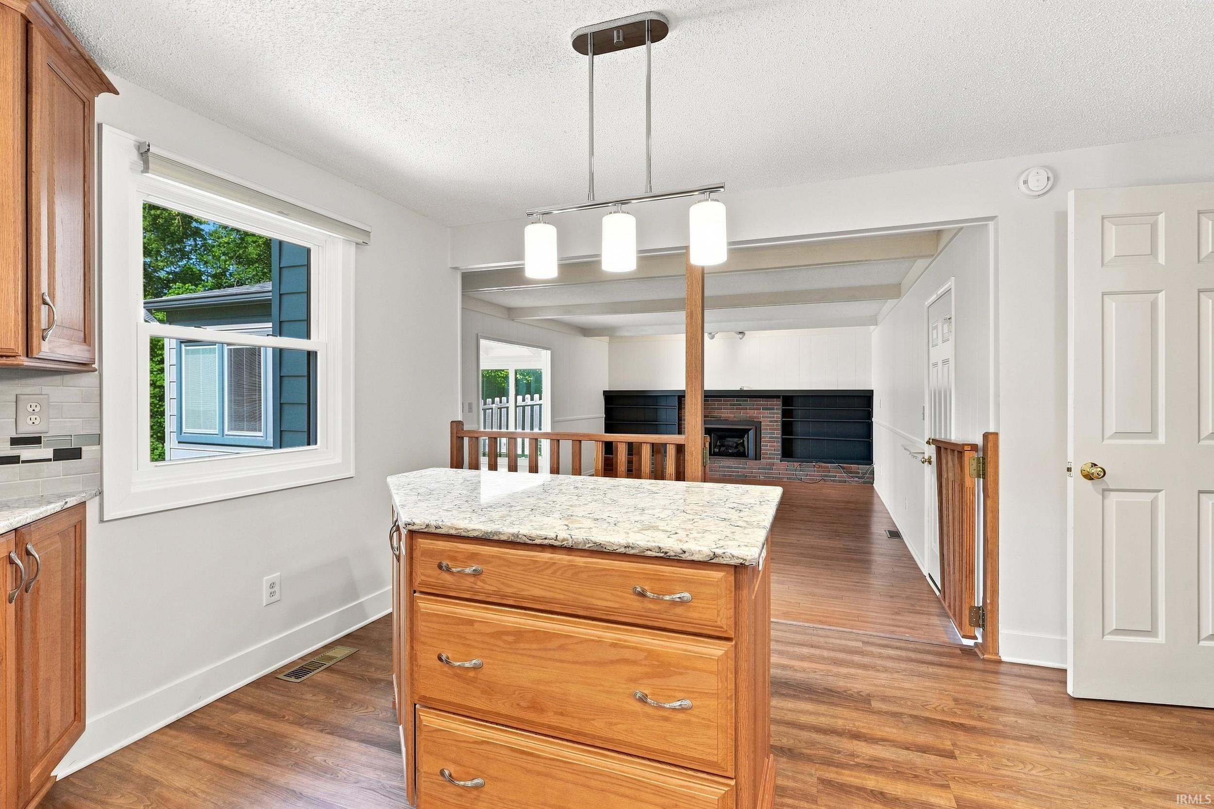 Open-concept kitchen and dining area featuring a wood-finish island with marble countertop and pendant lighting, custom wood cabinetry, hardwood flooring throughout, and seamless sightlines into the adjoining living spaces
