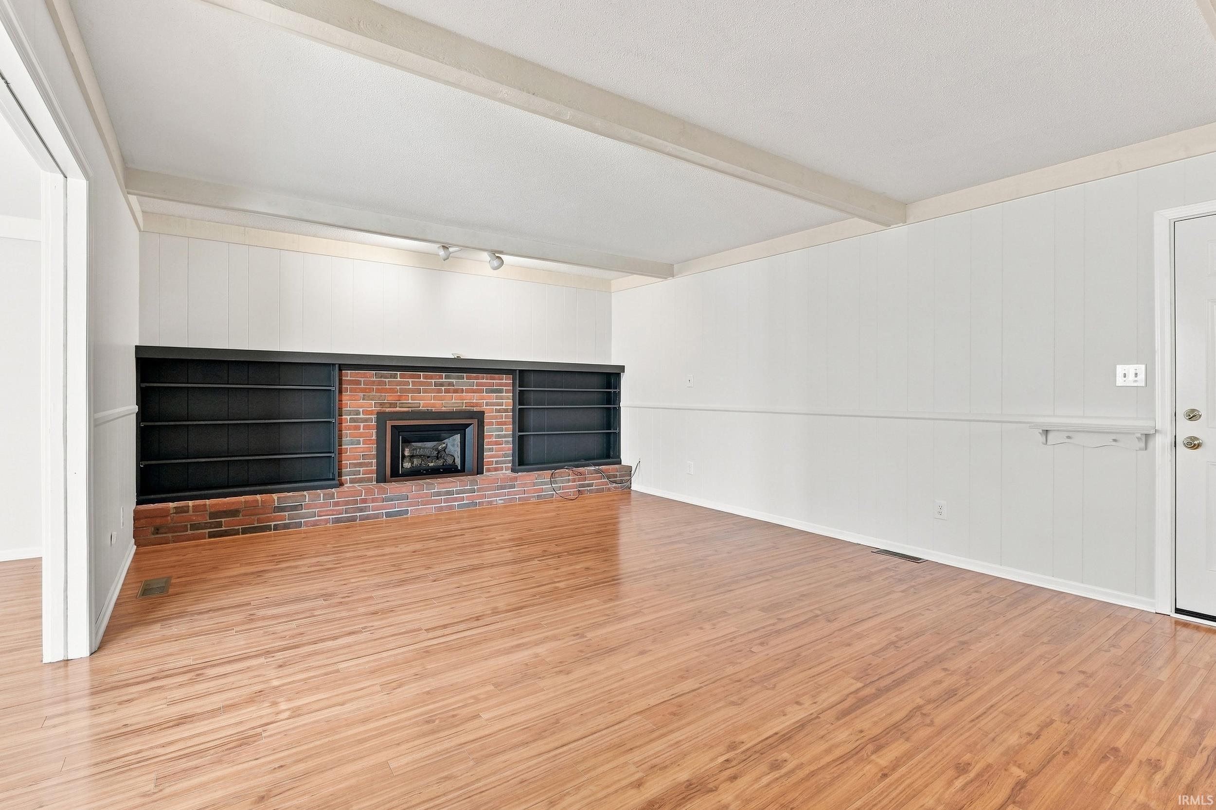 Spacious room featuring wood-finish flooring, a brick fireplace, and built-in shelving