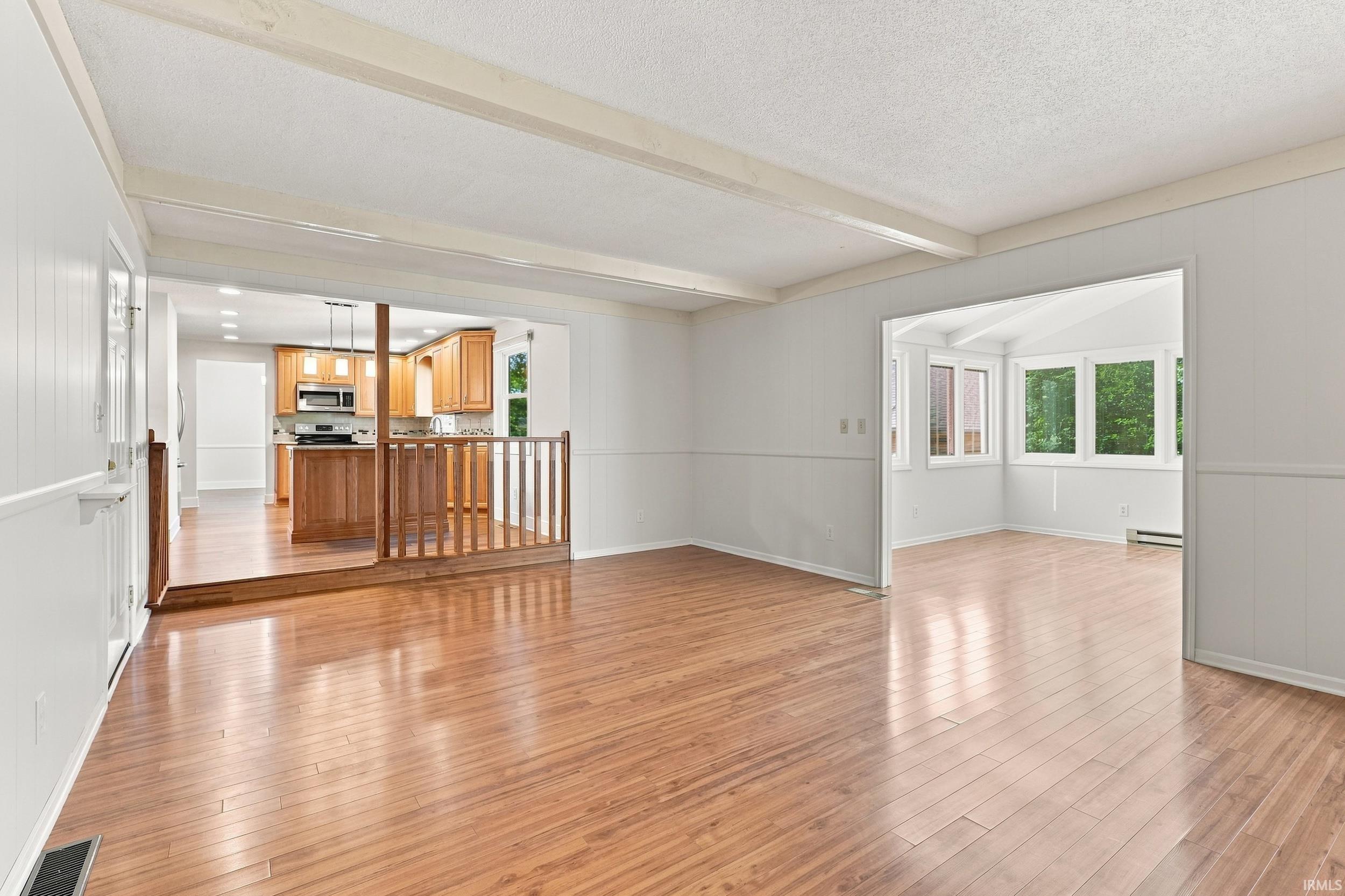 Expansive open-concept living area featuring wood-finish flooring, exposed ceiling beams, and a partial wood railing