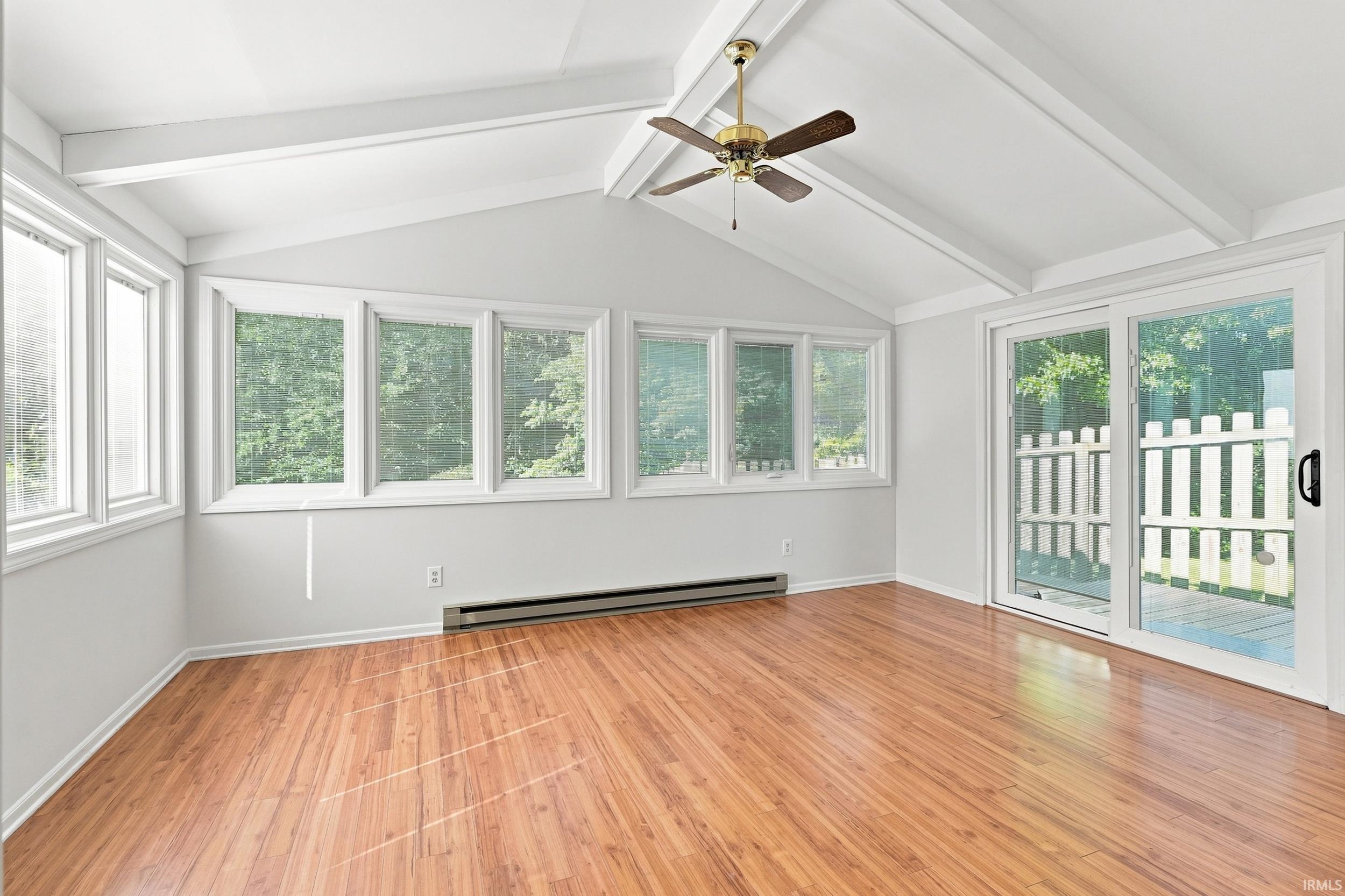 Bright and airy sunroom featuring soaring vaulted ceilings with exposed beams, hardwood flooring throughout, and abundant natural light from multiple casement windows