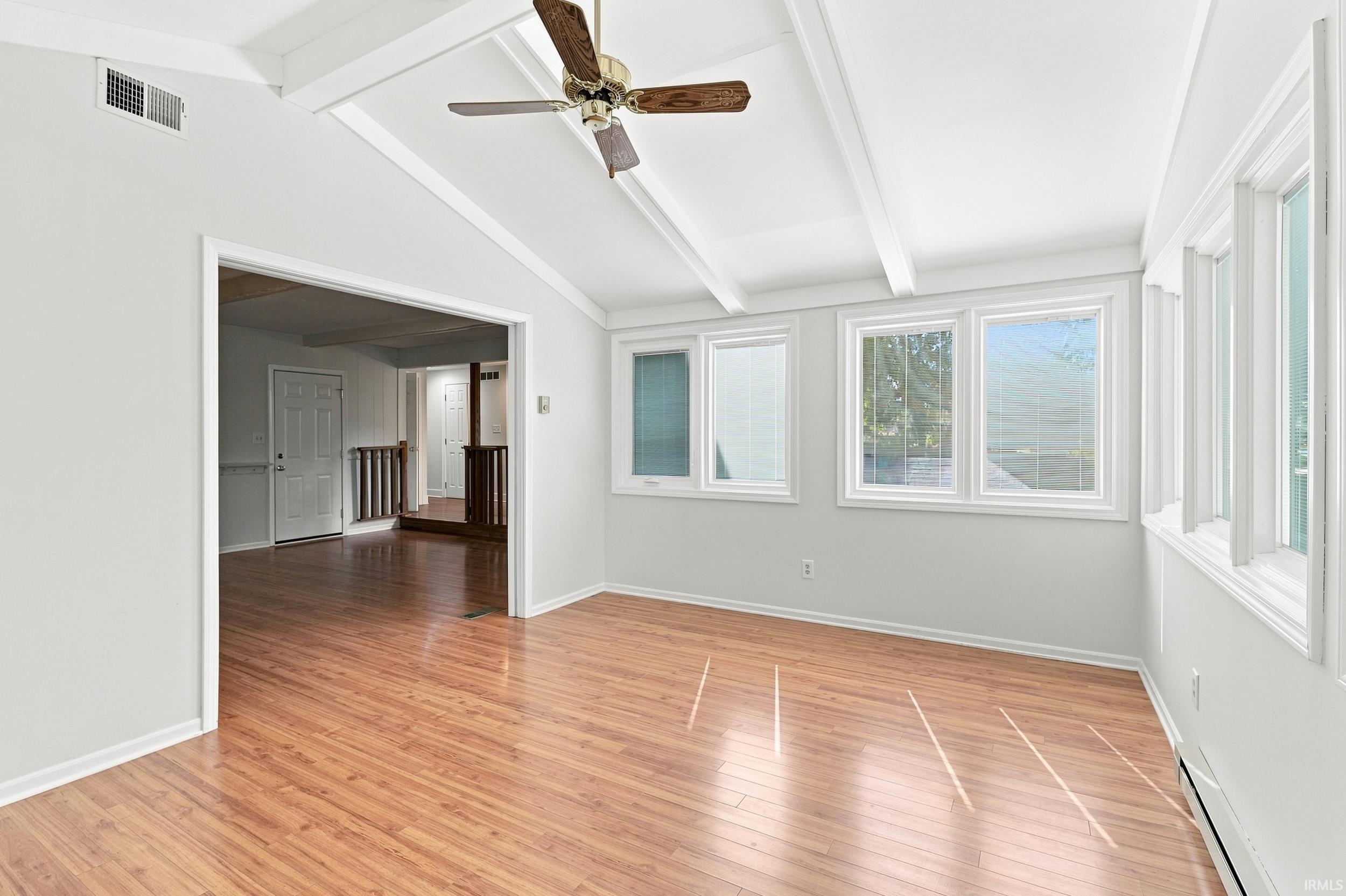 Bright interior space featuring wood-finish flooring, white walls, and a vaulted ceiling with exposed beams