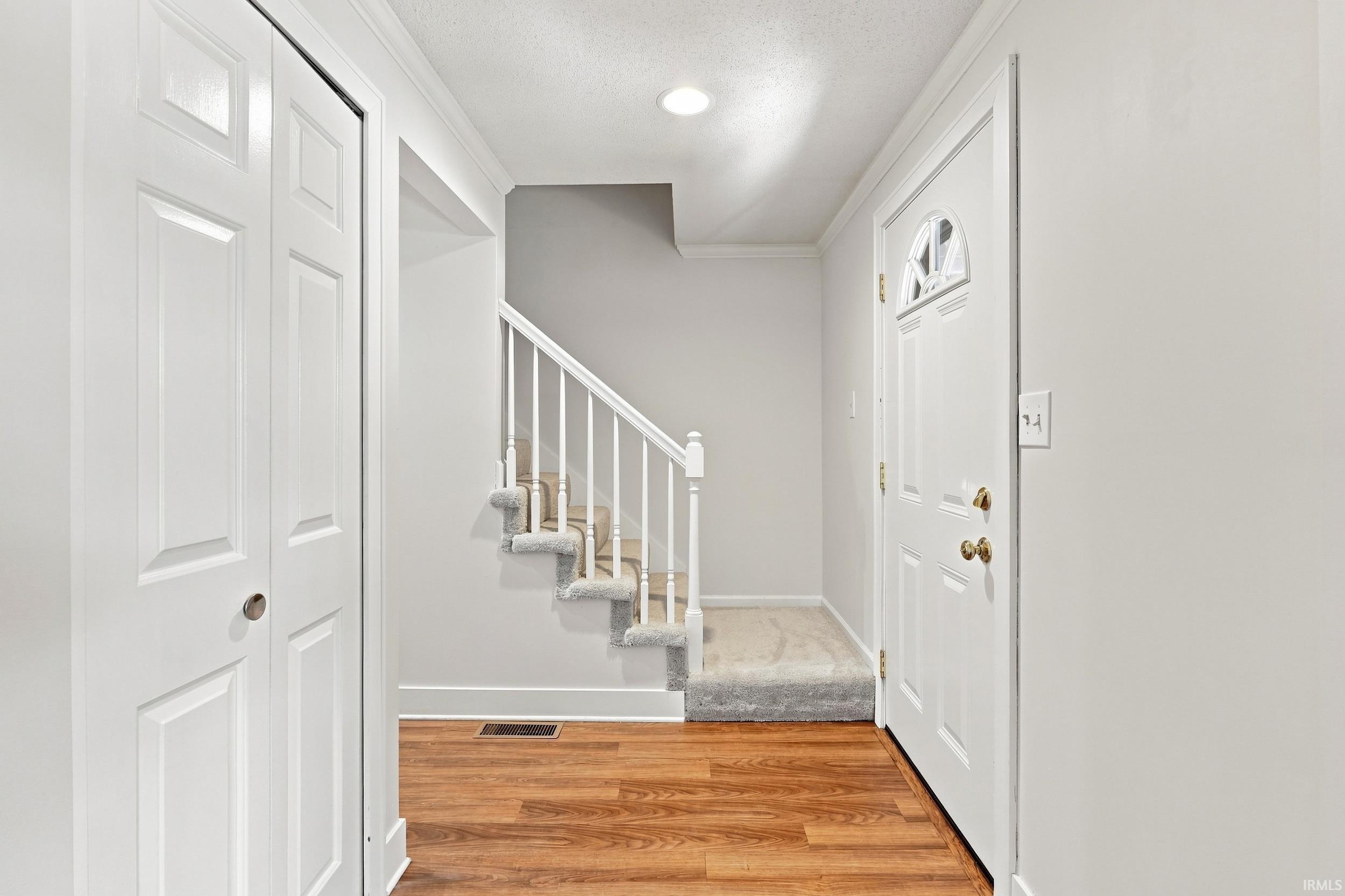 Welcoming entryway with wood-finish flooring, a white paneled front door with decorative glass, and a carpeted staircase featuring white balusters