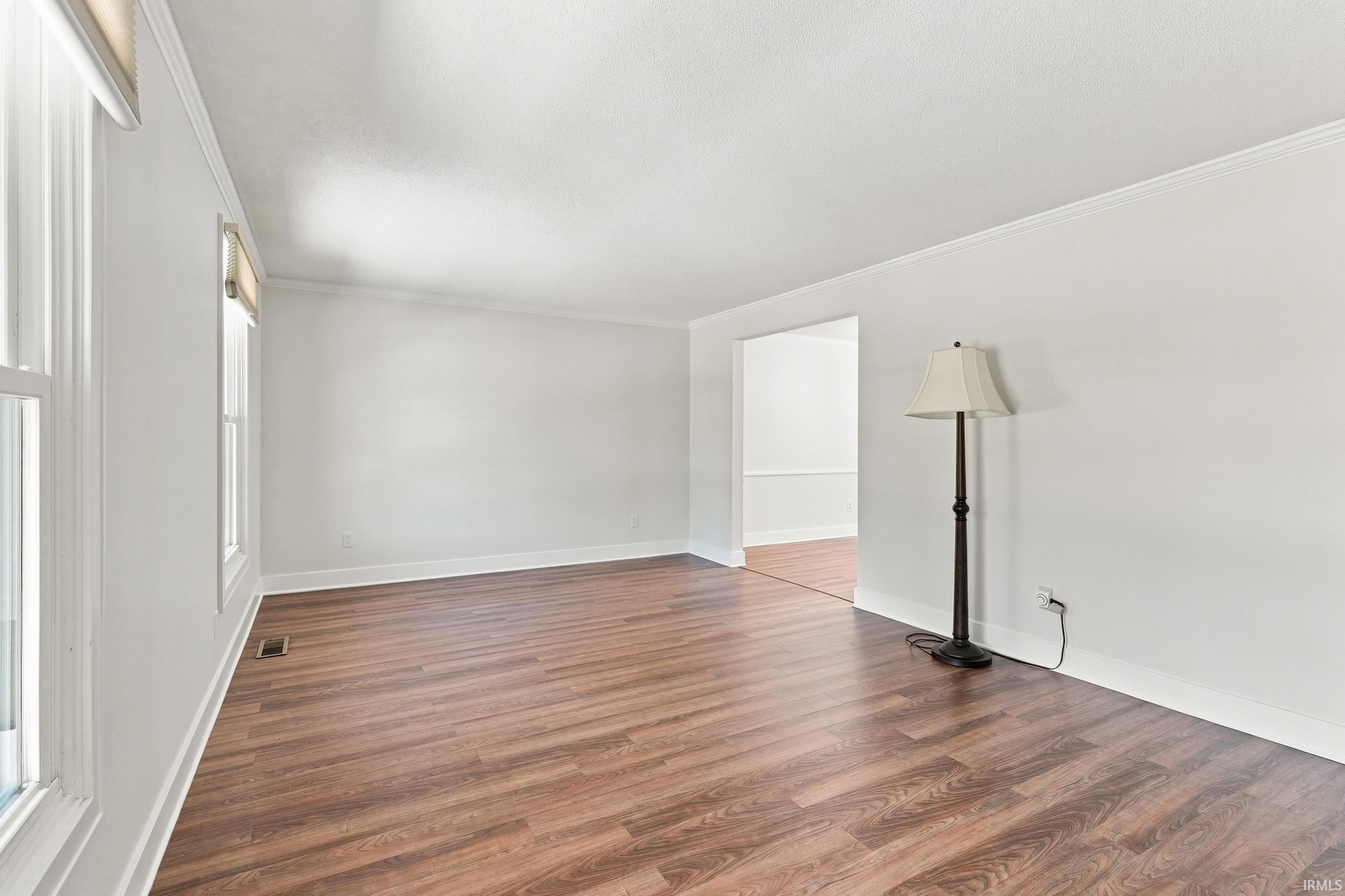 Spacious interior room featuring wood-finish flooring, white baseboards, and crown molding