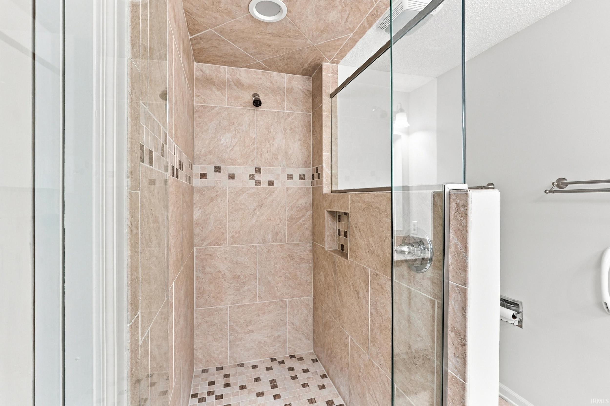 Spa-inspired walk-in shower featuring large-format travertine tile walls, decorative mosaic tile accents, rainfall showerhead, and frameless glass enclosure