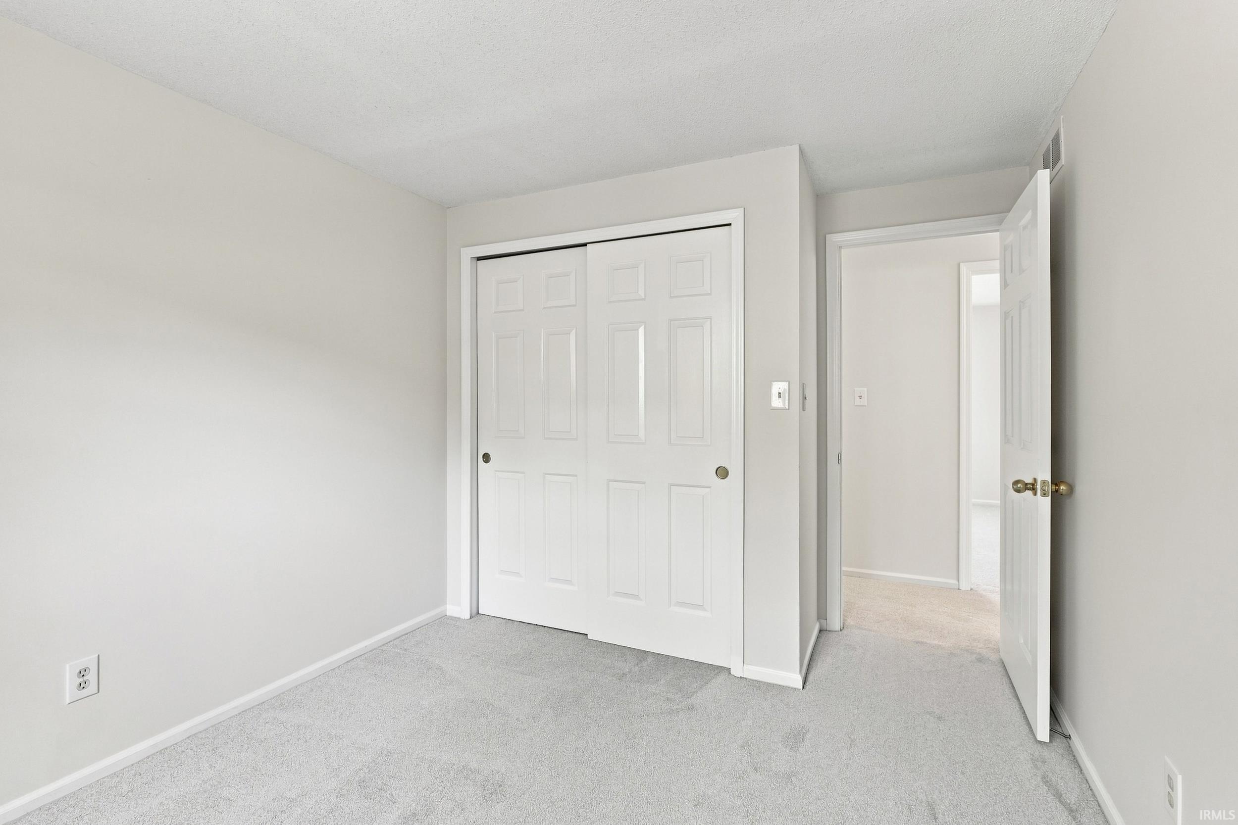 Spacious bedroom featuring dual sliding closet doors with six-panel design, neutral carpet flooring, and bright natural lighting from multiple windows