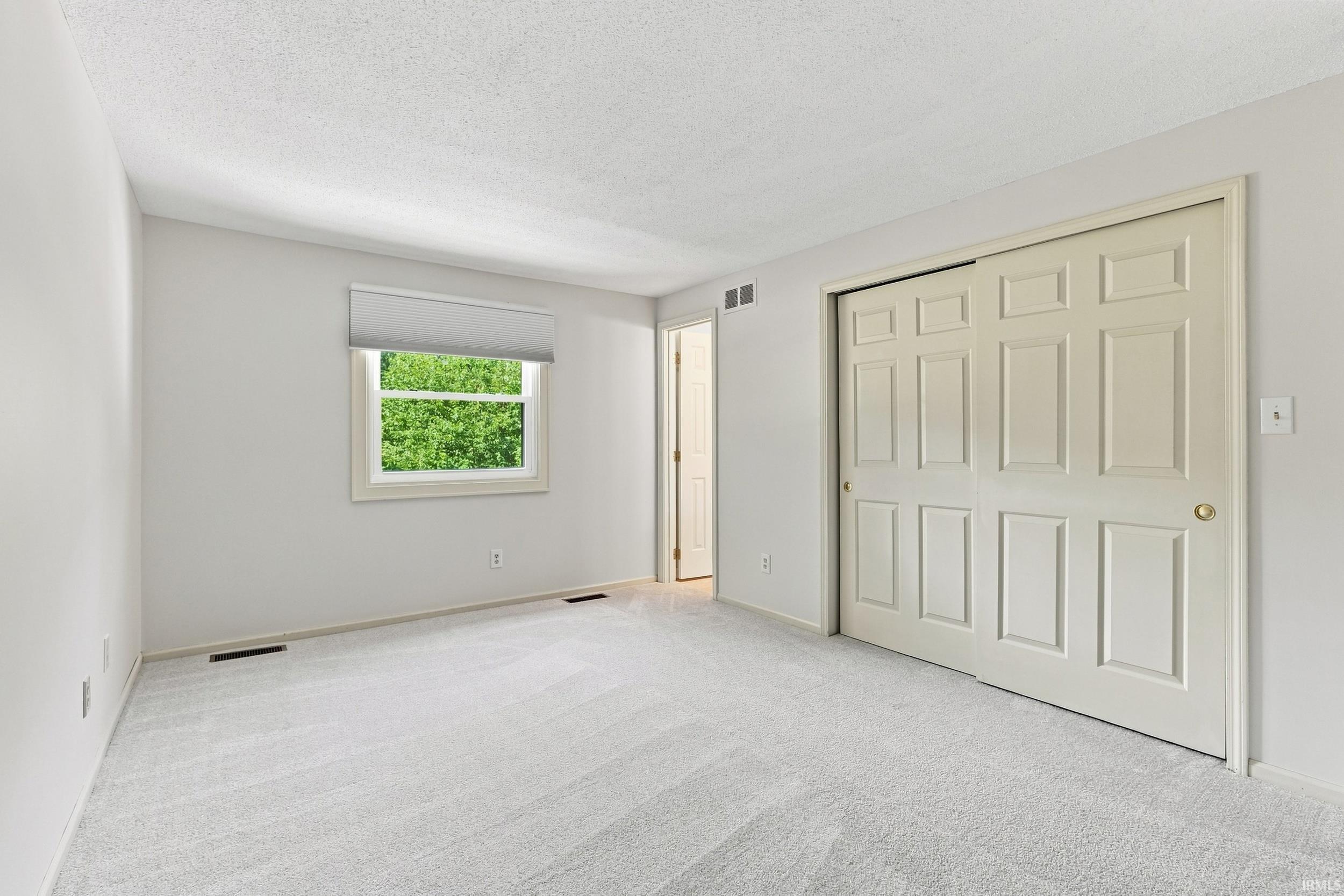 Neutral-toned room featuring light gray carpeting, white walls, and a white window frame with a roller shade