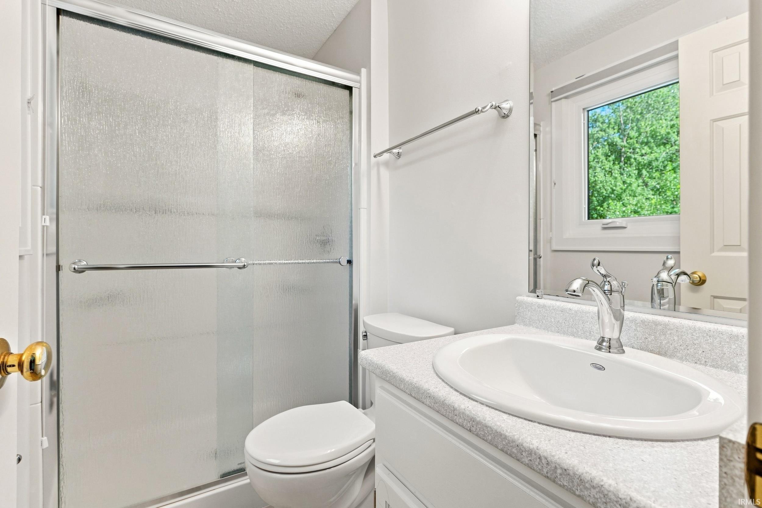 Bright, updated bathroom featuring a frameless glass-enclosed shower with sliding door, dual-sink vanity with light-finish countertop, white porcelain toilet, and chrome fixtures