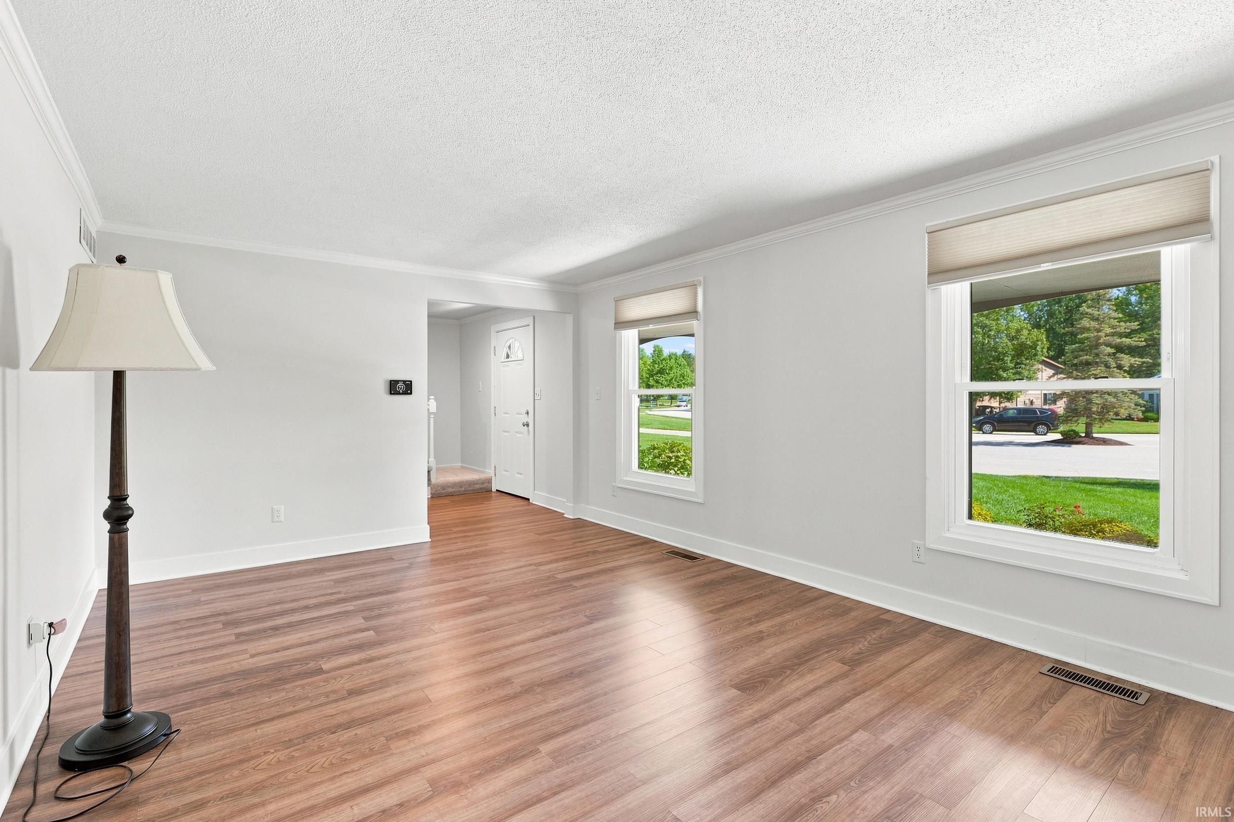 Bright room featuring wood-finish flooring, crisp white walls, and multiple windows with roller shades