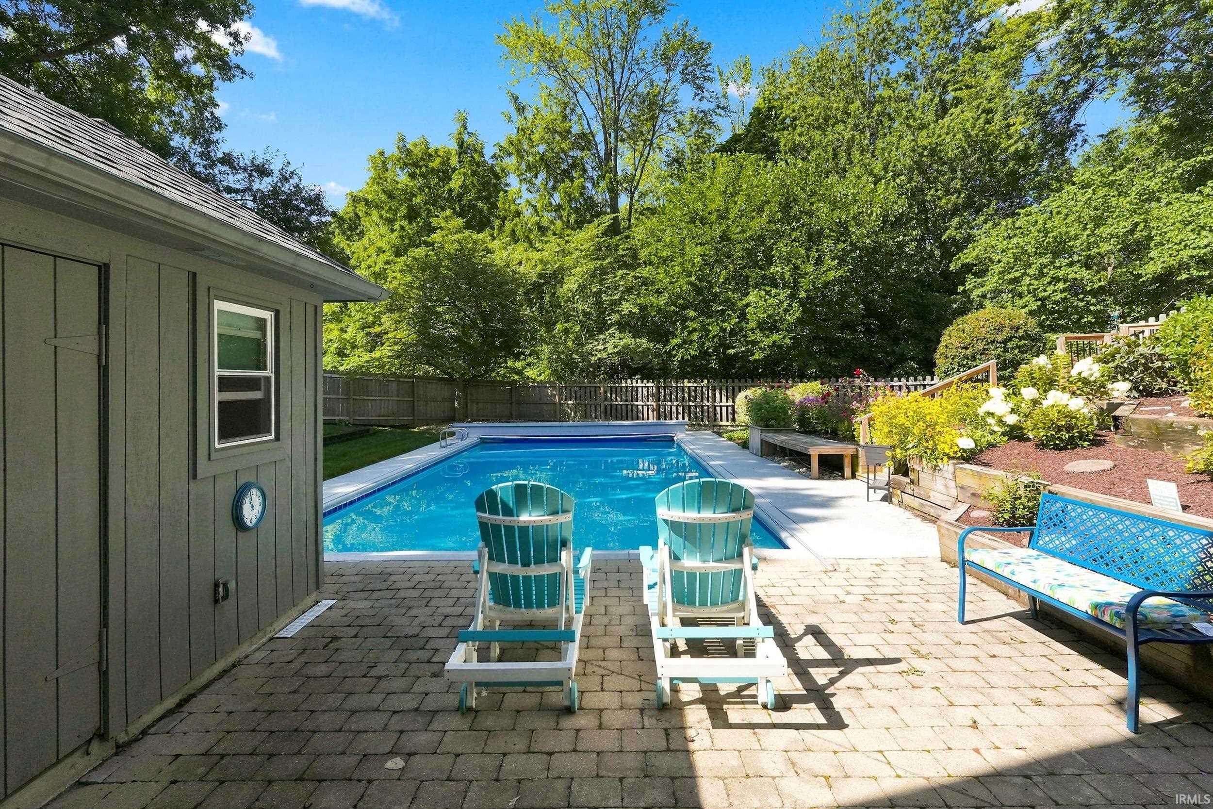 Resort-style backyard oasis featuring an in-ground swimming pool with crystal-clear water, complemented by Adirondack lounge chairs on a permeable paver patio