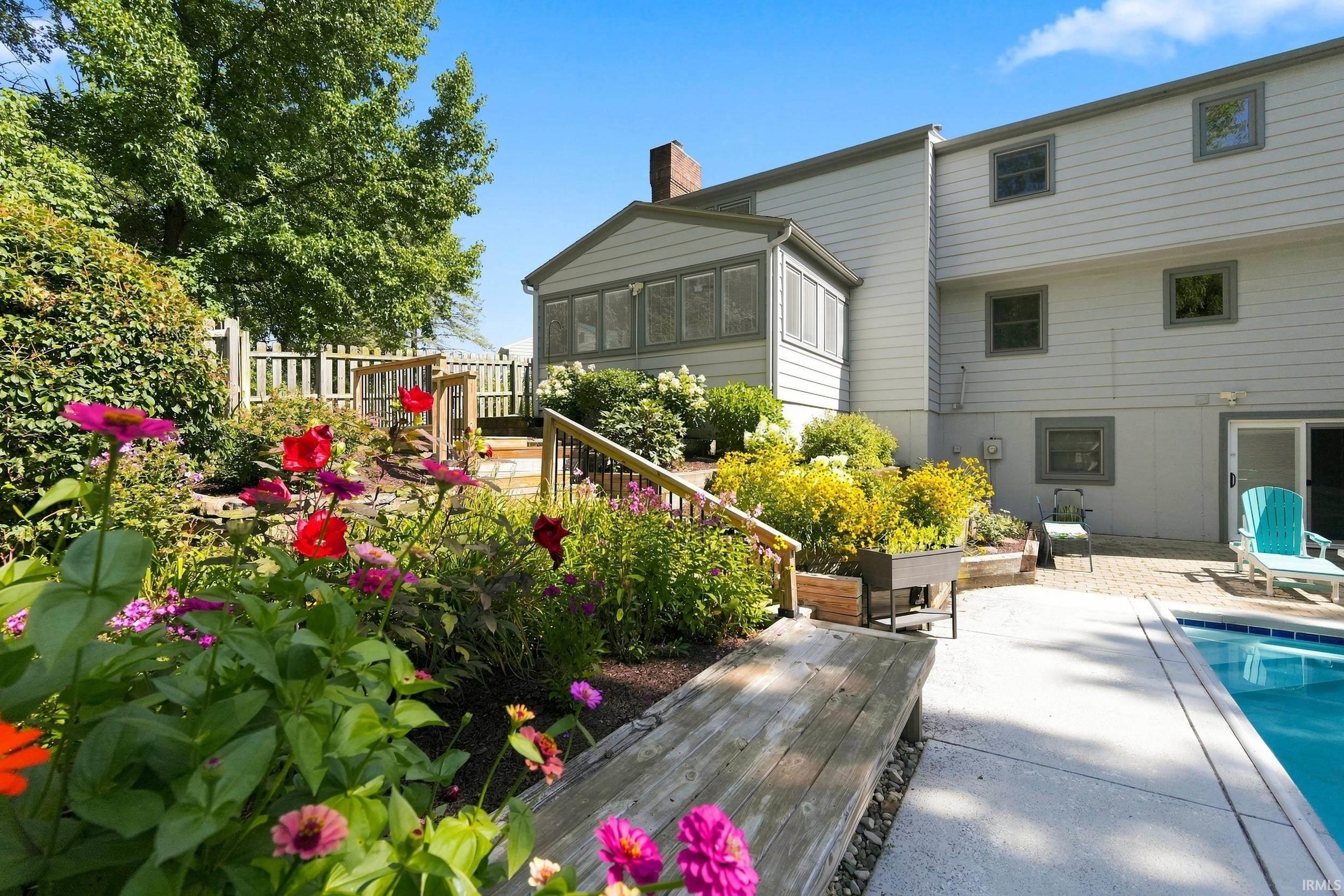 Expansive backyard oasis featuring a vibrant perennial garden, a multi-level wooden deck with railings, an in-ground swimming pool, and a screened-in porch