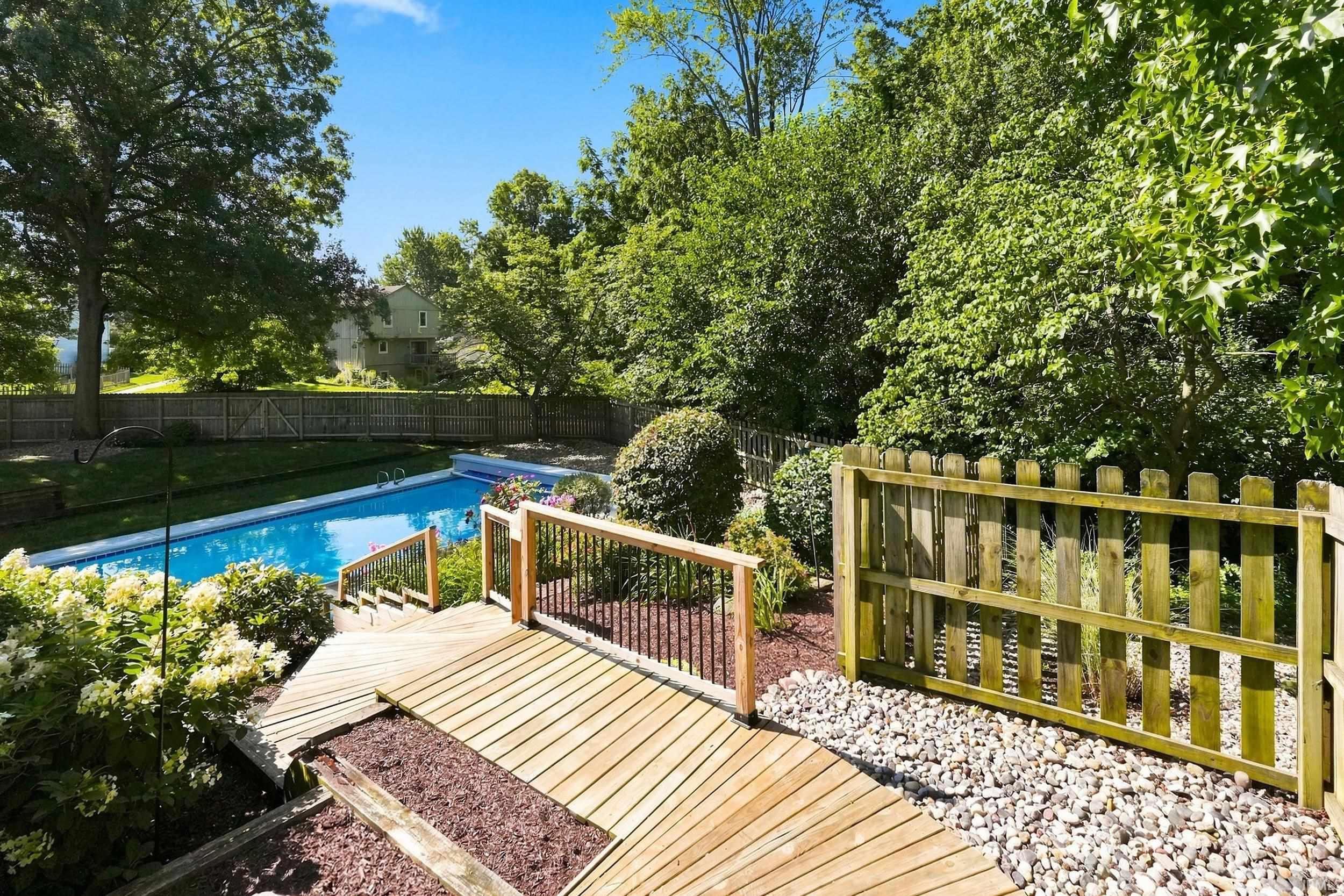 Backyard oasis featuring an in-ground swimming pool with safety fencing, multi-level composite decking, and mature landscaping