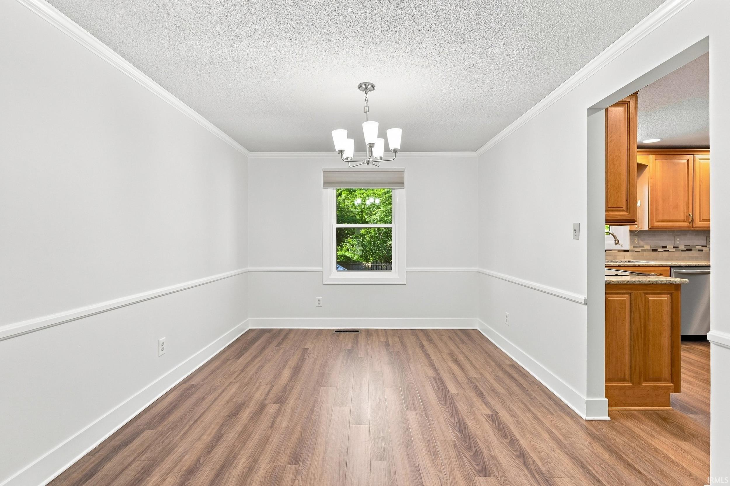 Spacious room featuring wood-finish flooring, white walls with chair rail and crown molding, and a contemporary chandelier