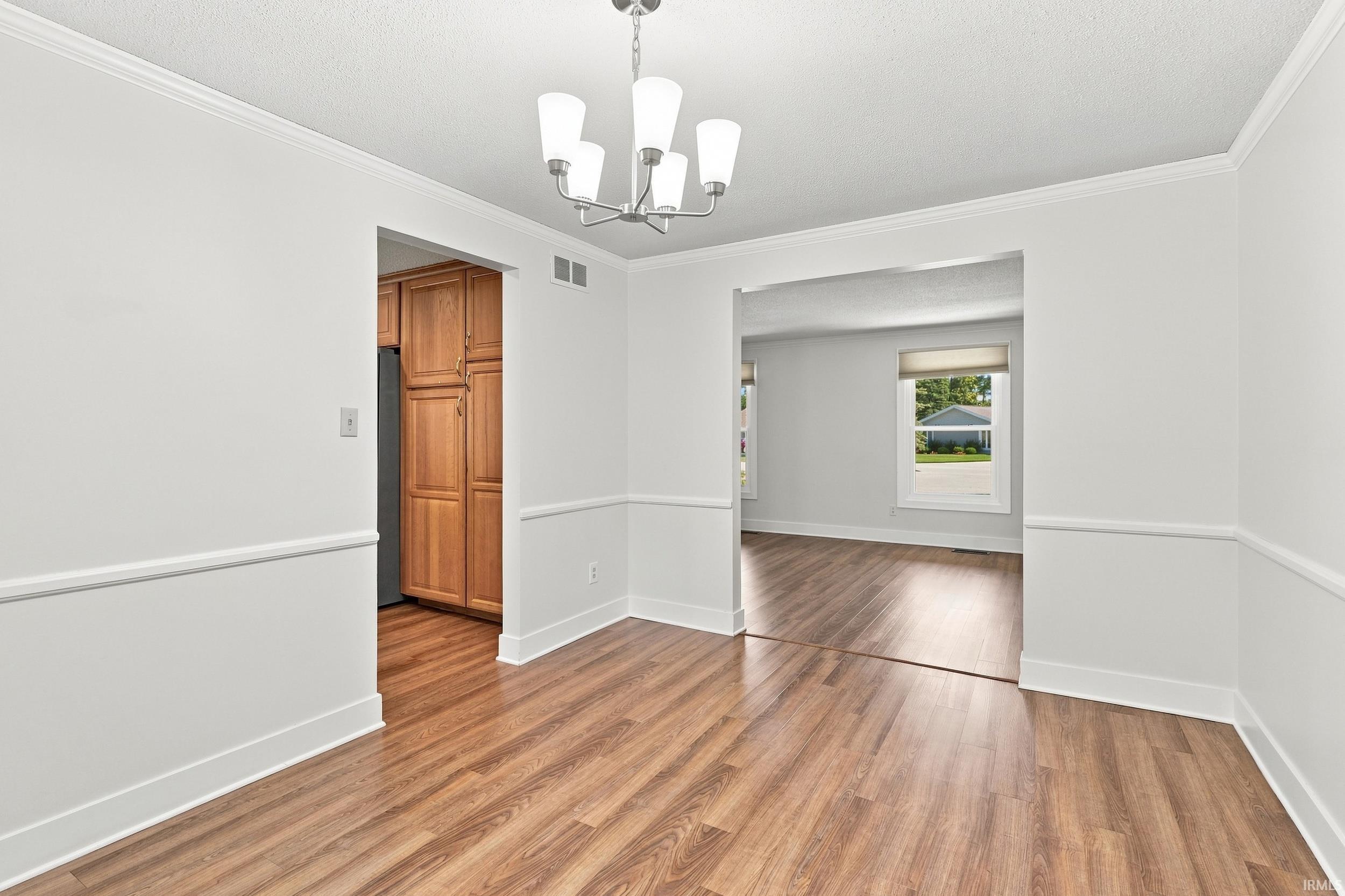Elegant foyer showcasing pristine white walls with classic wainscoting, rich wood-finish flooring throughout, and a contemporary chandelier