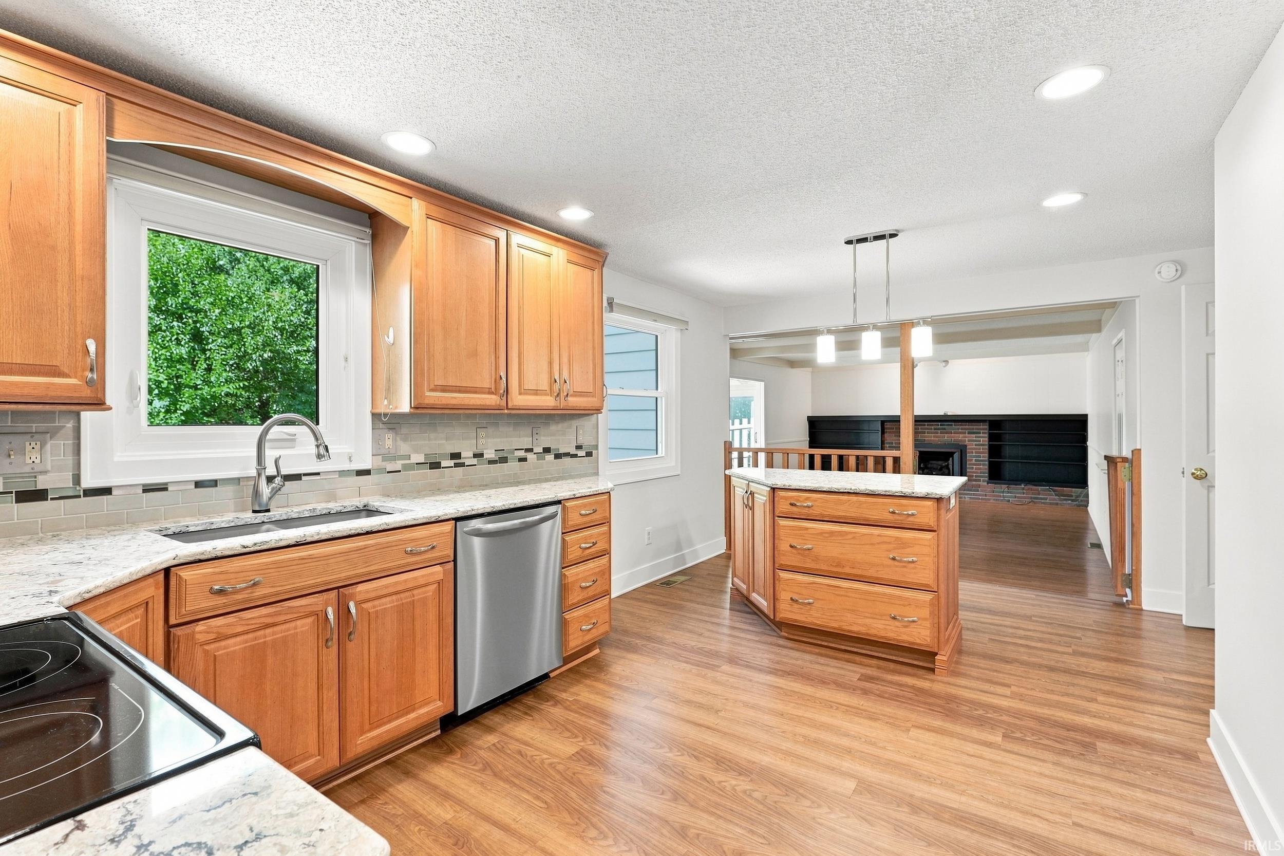 Kitchen with wood-finish flooring, light wood cabinetry, white stone countertops, and a tile backsplash