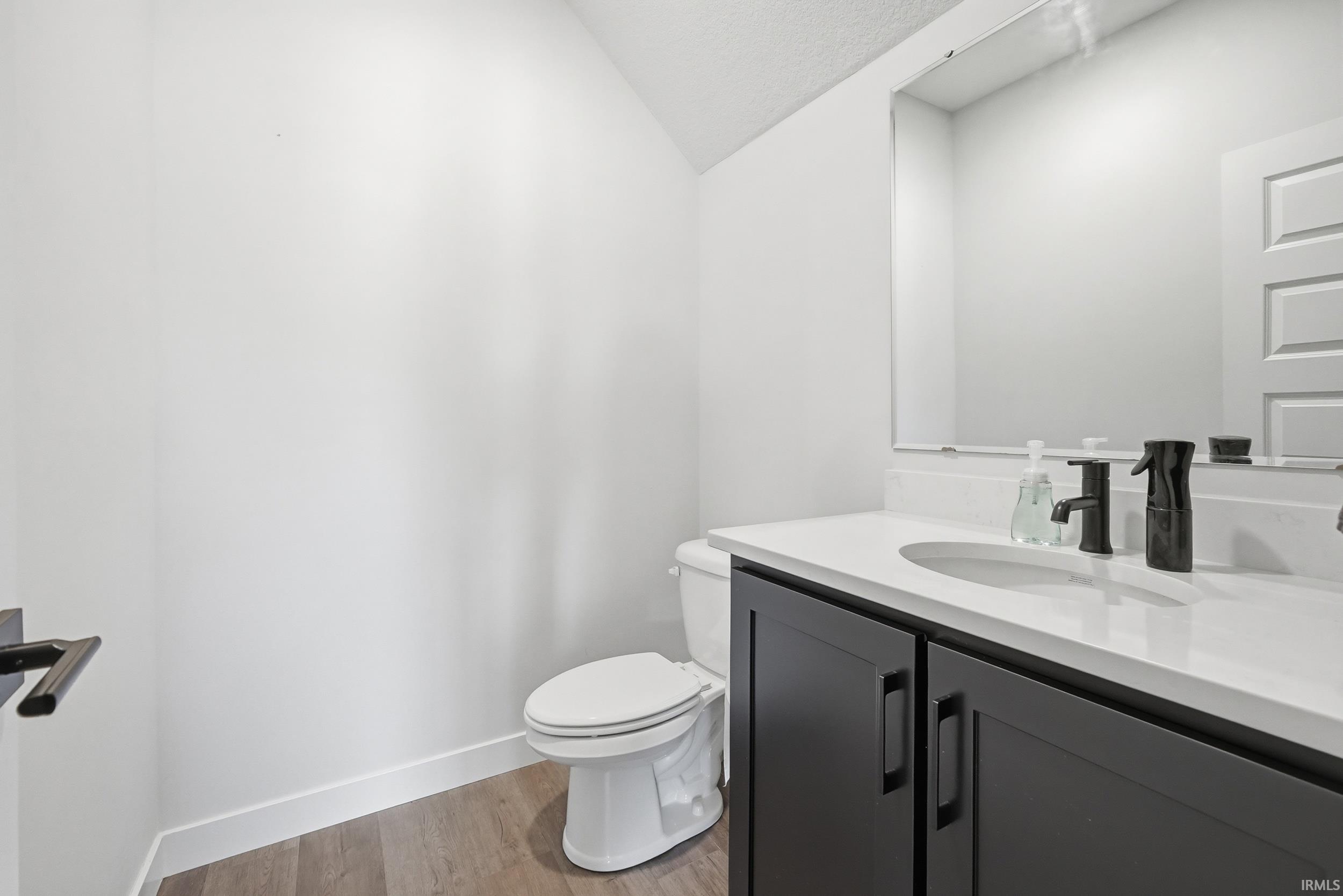 Modern powder room featuring a white vanity with an integrated sink, black cabinetry, matte black fixtures, a white toilet, and wood-finish flooring