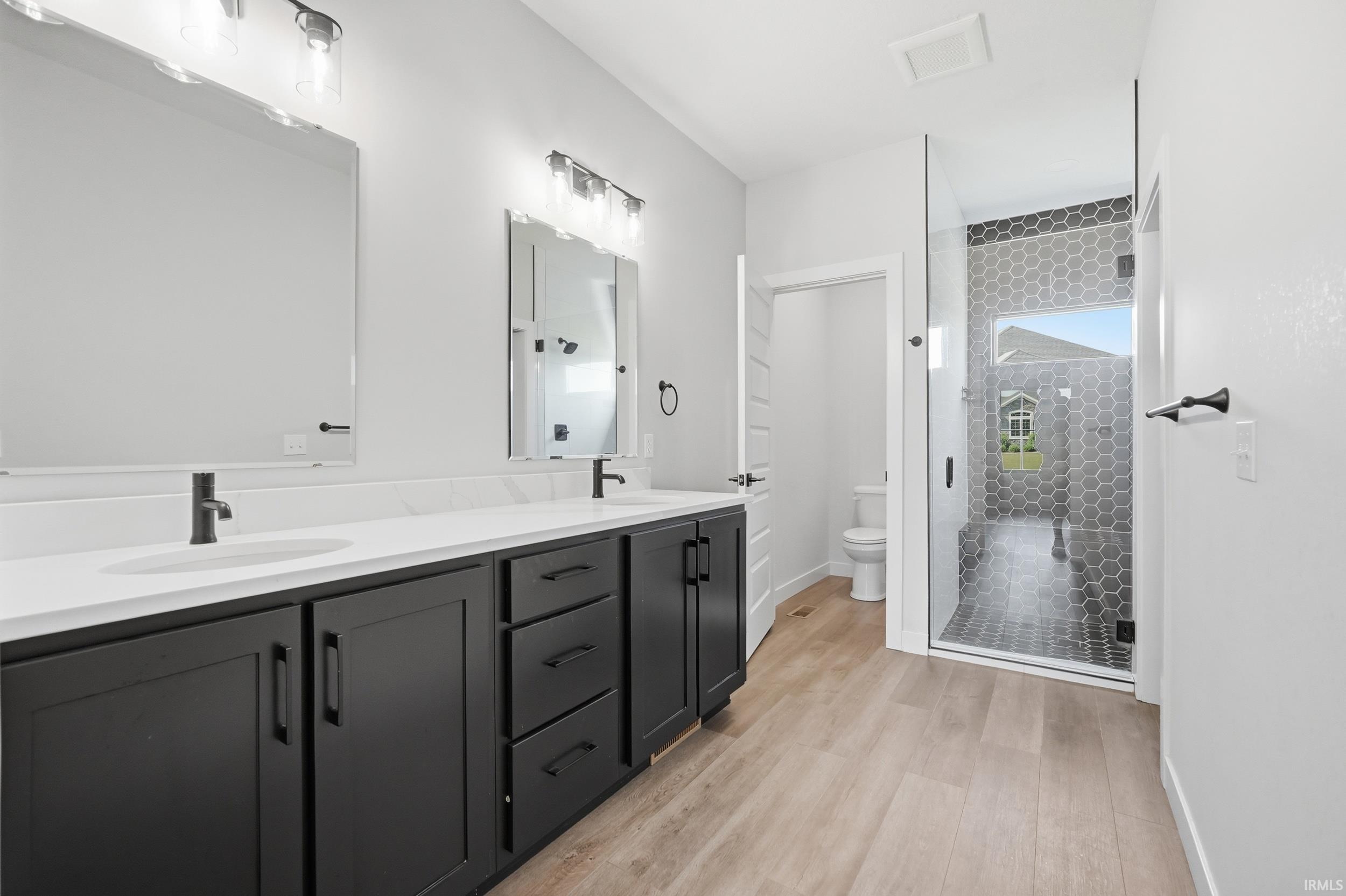 Dual vanity with matte black hardware and white countertops, featuring wood-finish flooring