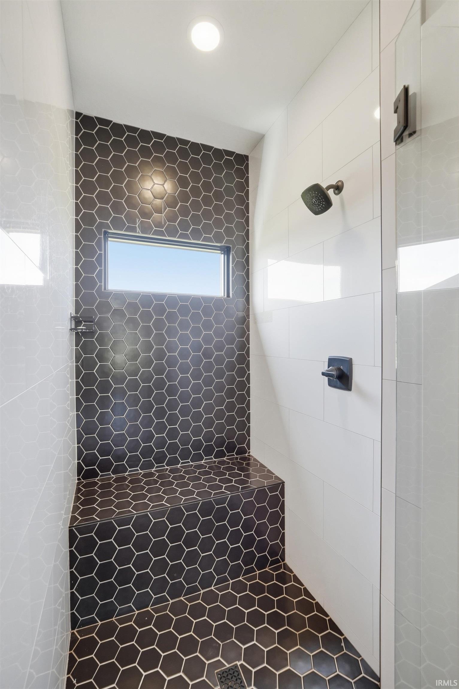 Modern shower featuring black hexagonal tile, a built-in bench, a horizontal window, matte black fixtures, and white subway tile accents