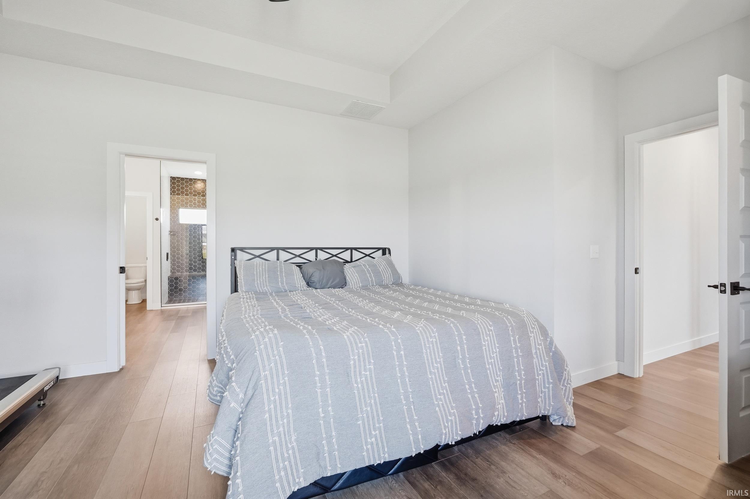 Spacious room featuring wood-finish flooring, white walls, and a tray ceiling
