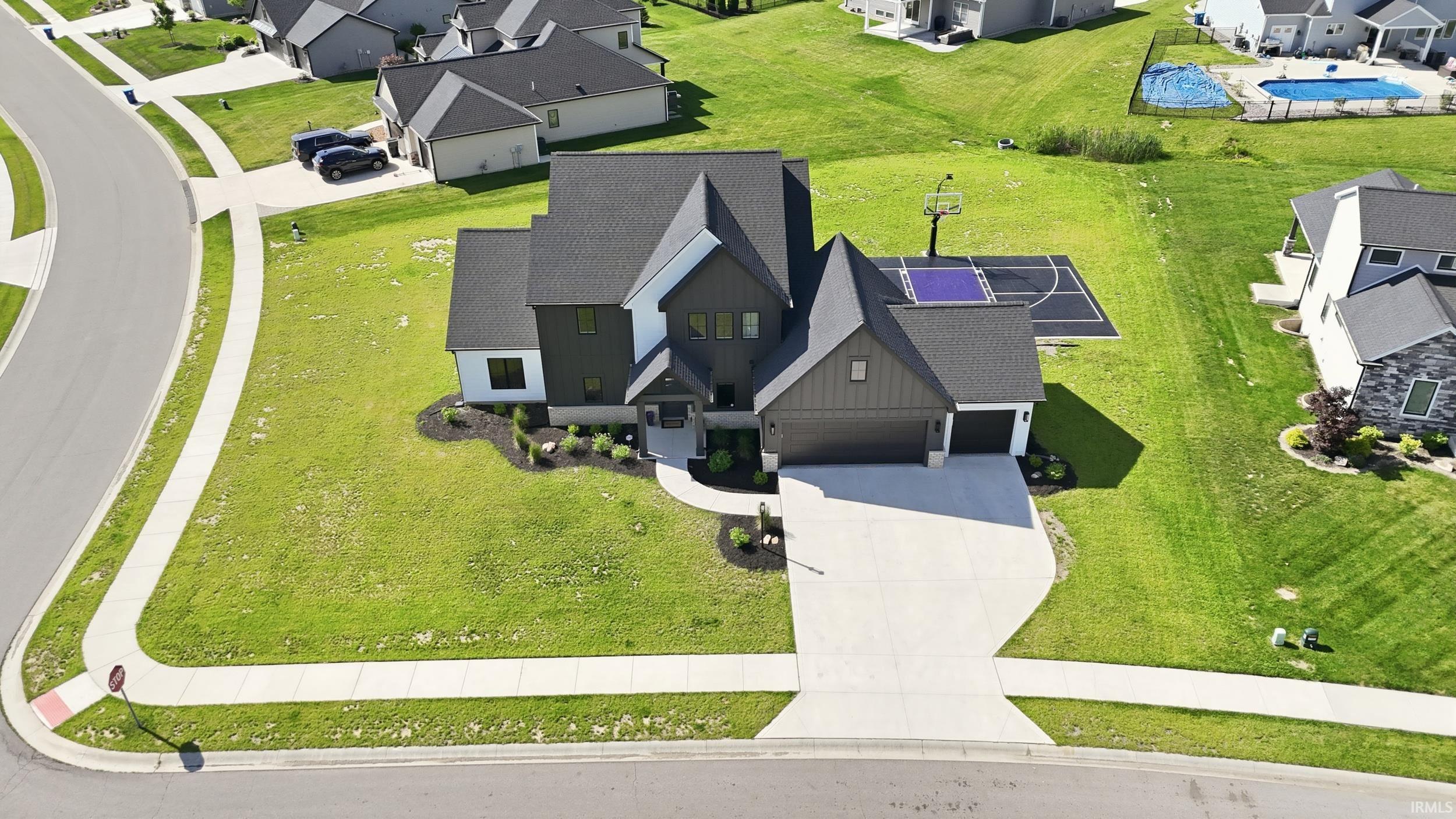 Modern two-story residence featuring a dark-toned exterior with contrasting white accents, a two-car garage, concrete driveway, and an adjacent sports court