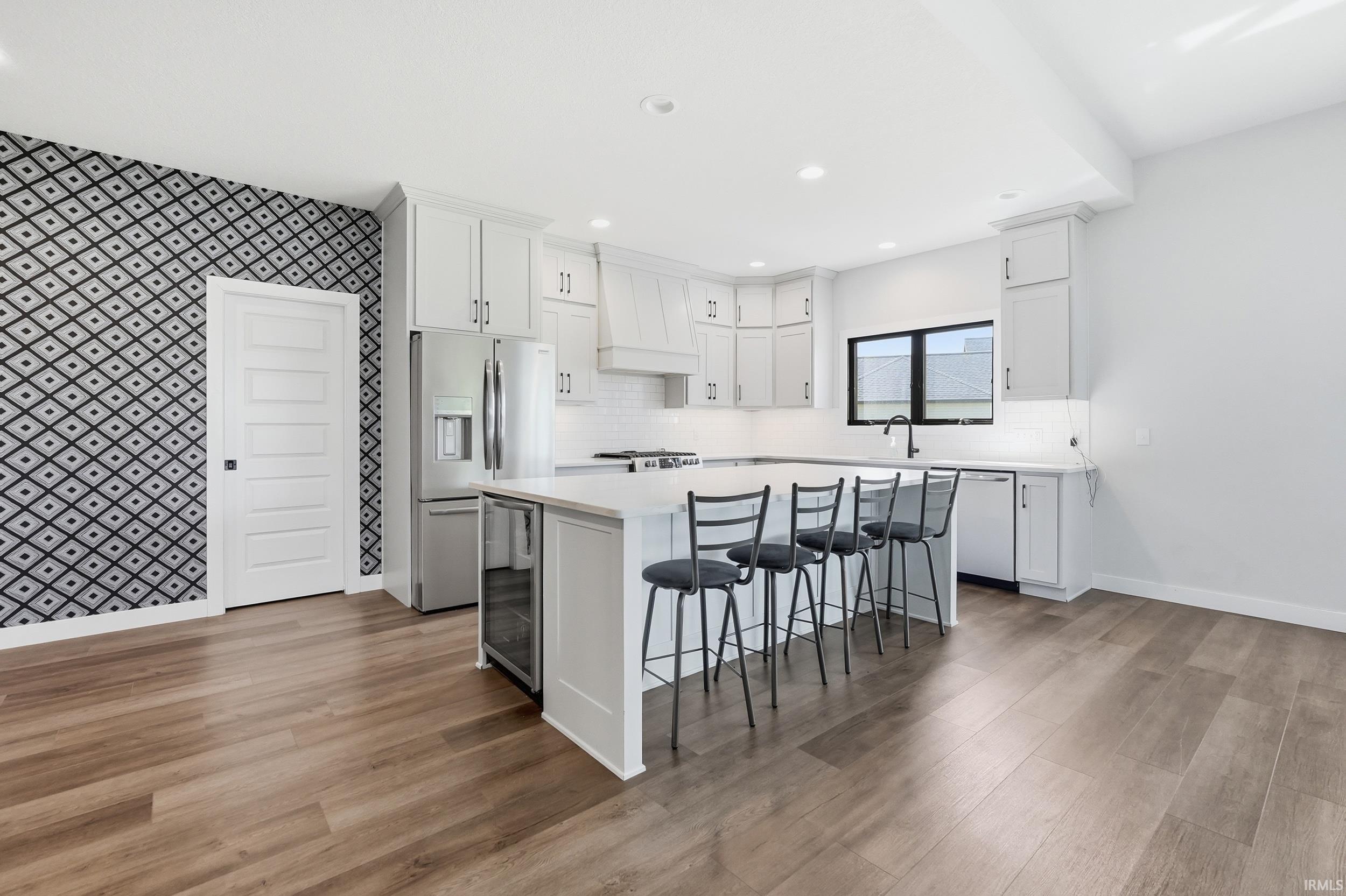 Bright kitchen featuring an expansive center island with seating, stainless steel appliances, white cabinetry, and wood-finish flooring