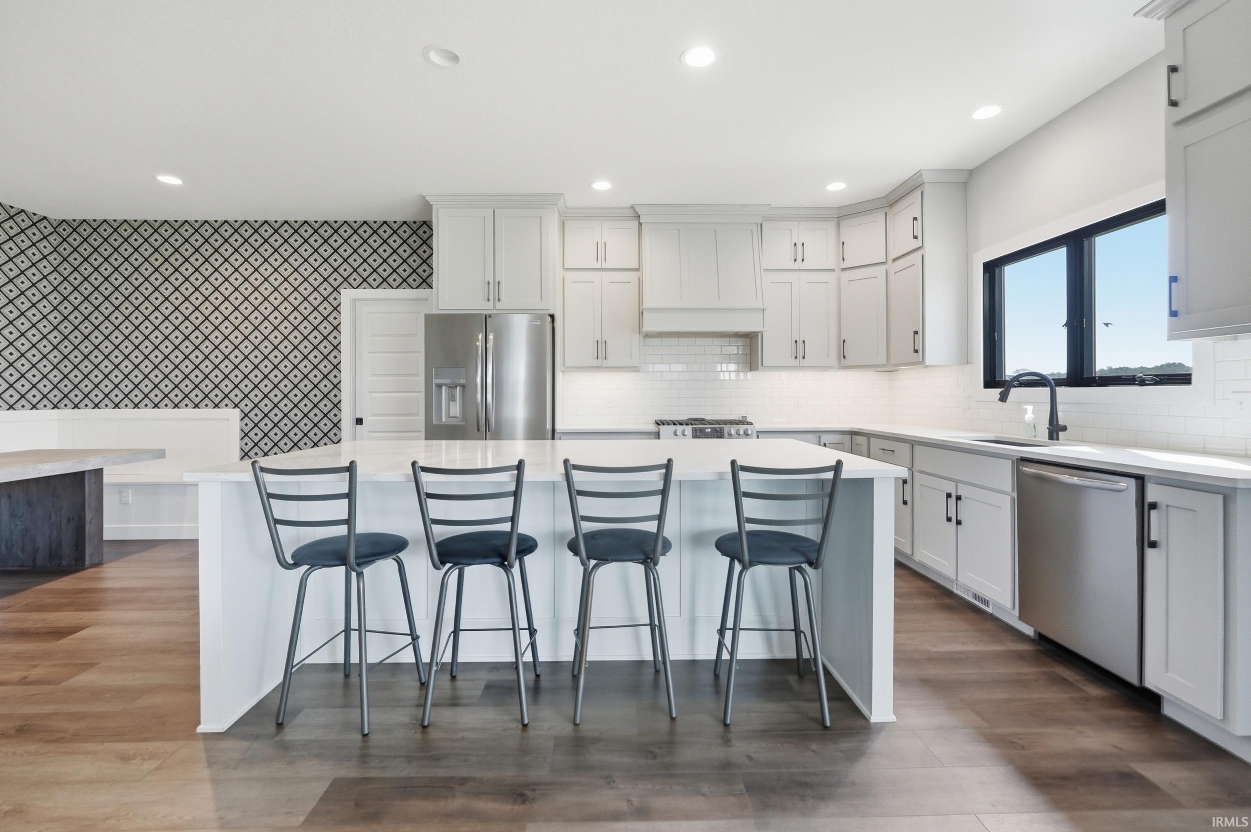 Open-concept kitchen featuring an island with seating, stainless steel appliances, light-toned cabinetry, subway tile backsplash, and wood-finish flooring