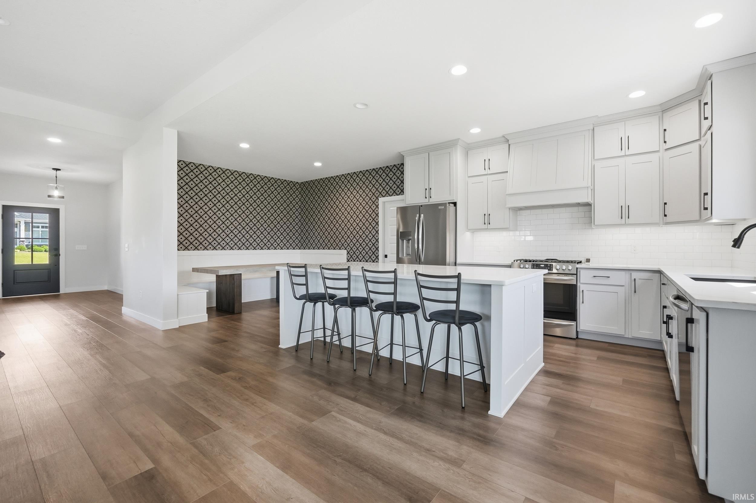Bright kitchen featuring white shaker cabinetry, stainless steel appliances, a center island with seating, a subway tile backsplash, and wood-finish flooring