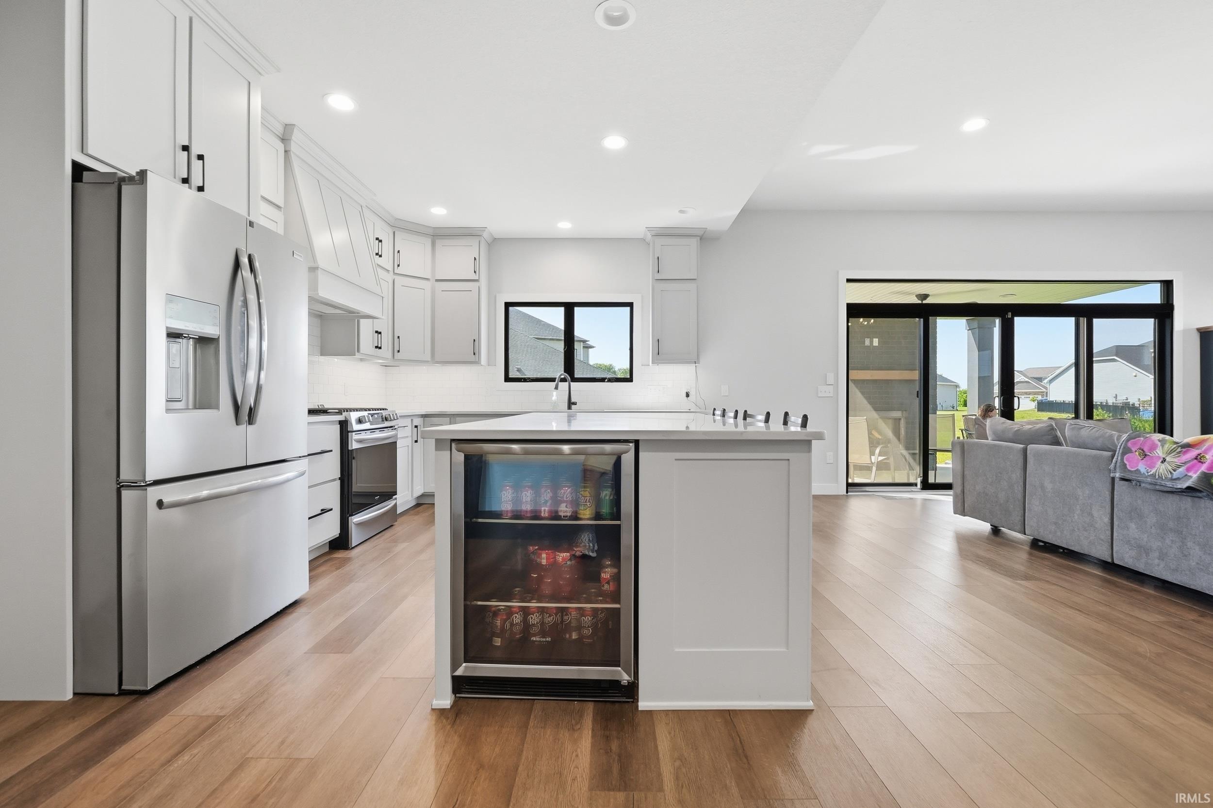 Kitchen featuring light-toned cabinetry, stainless steel appliances, a center island with integrated beverage cooler, and wood-finish flooring