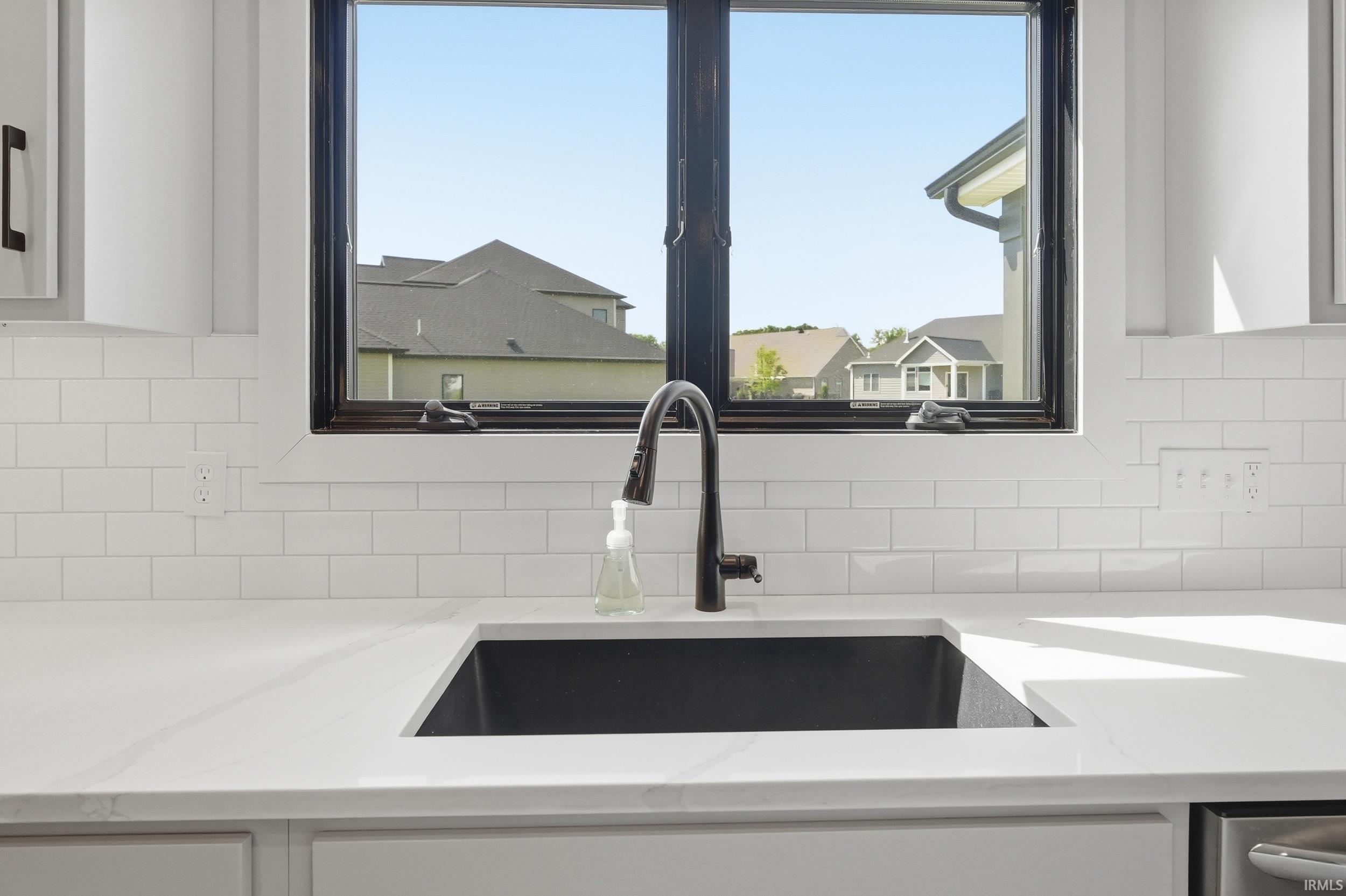 White subway tile backsplash with a black framed window, a large black sink, and a matte black pull-down faucet