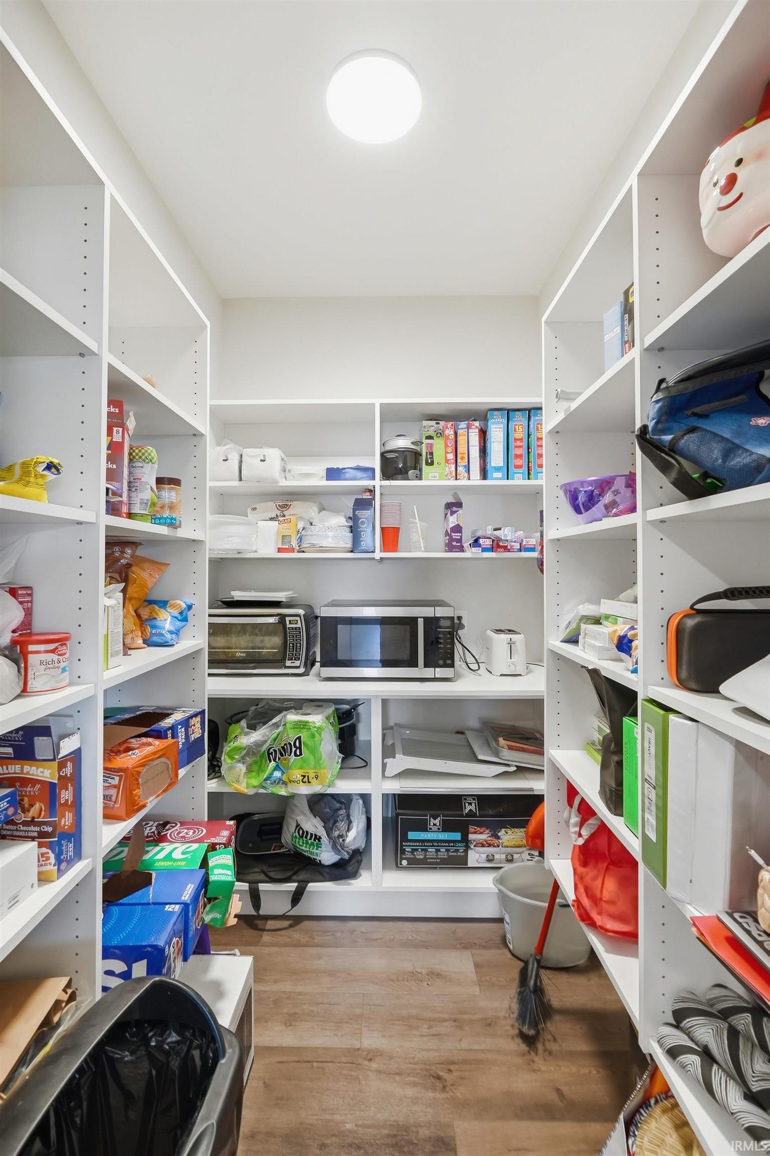 Walk-in pantry featuring extensive white shelving, wood-finish flooring, and recessed ceiling lighting