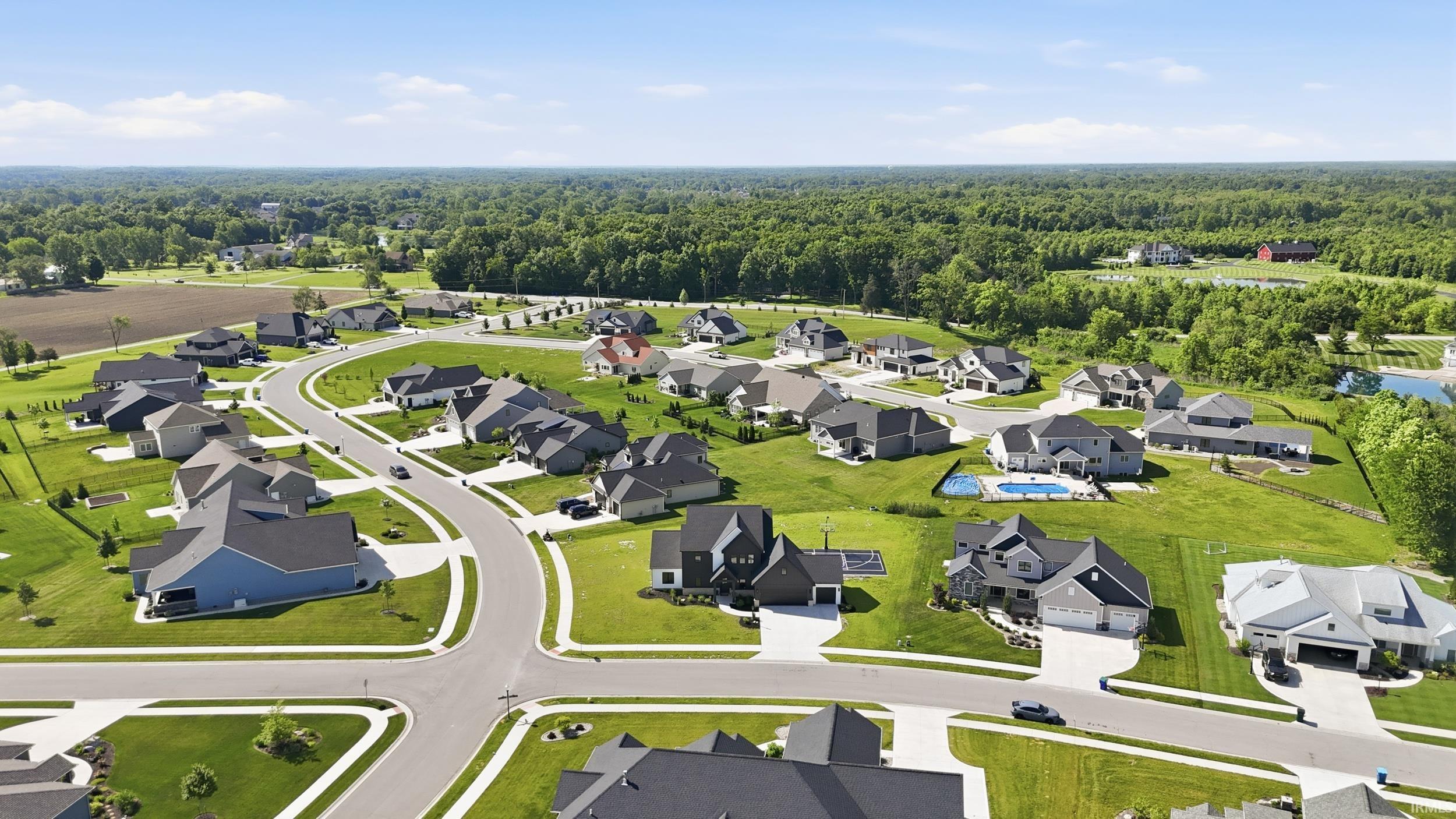 Aerial view of a residential community featuring a curved street layout, individual single-family homes with diverse architectural styles, and expansive green lawns