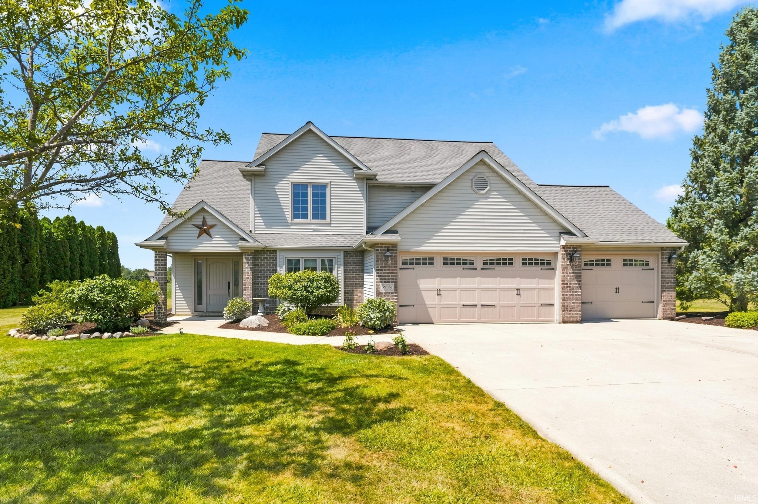 Impressive two-story colonial home featuring a three-car garage, brick and siding exterior, and a professionally landscaped front lawn with mature trees and established plantings