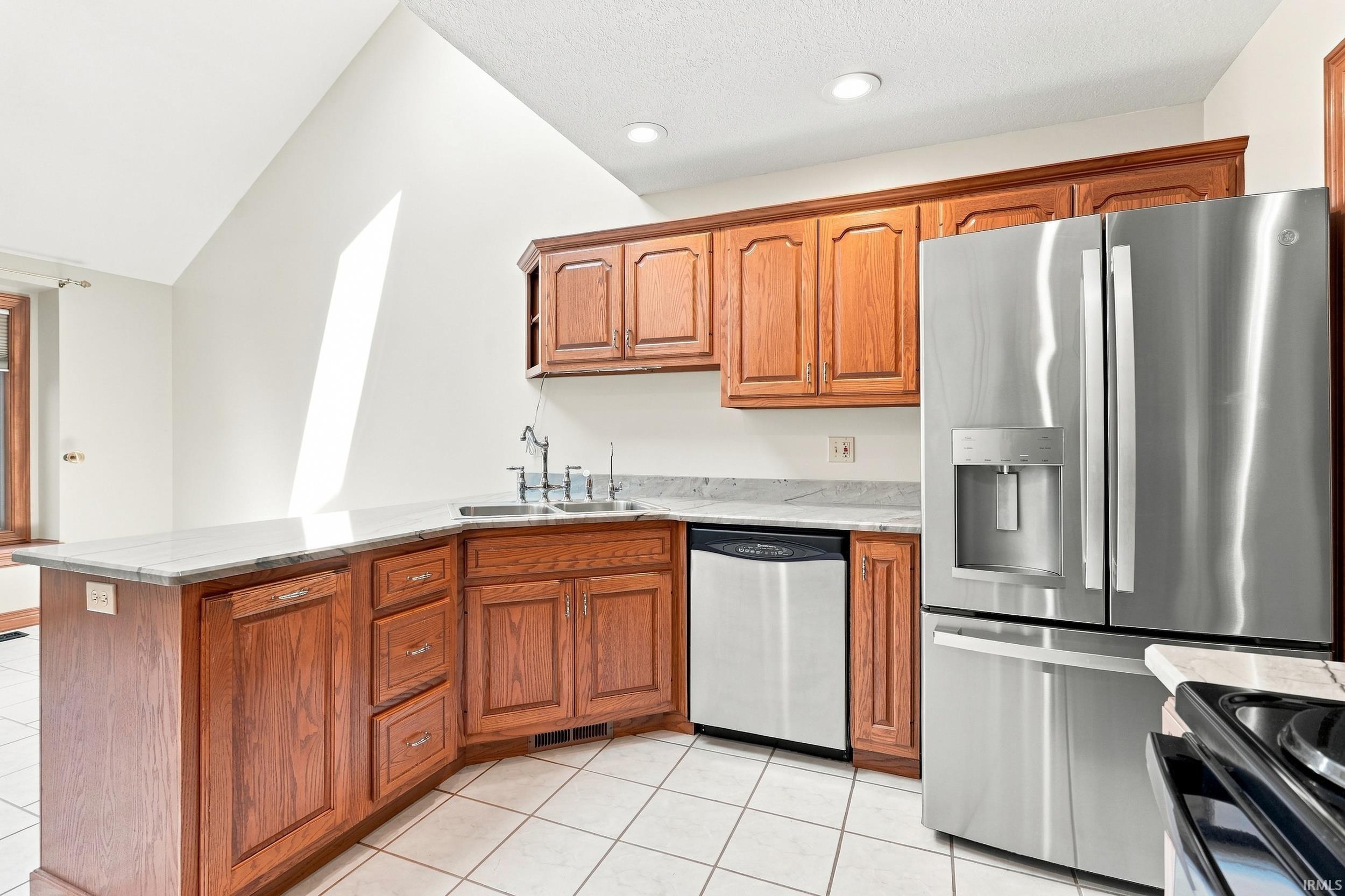 Kitchen featuring wood cabinetry, stainless steel appliances, white tile flooring, and light-toned countertops