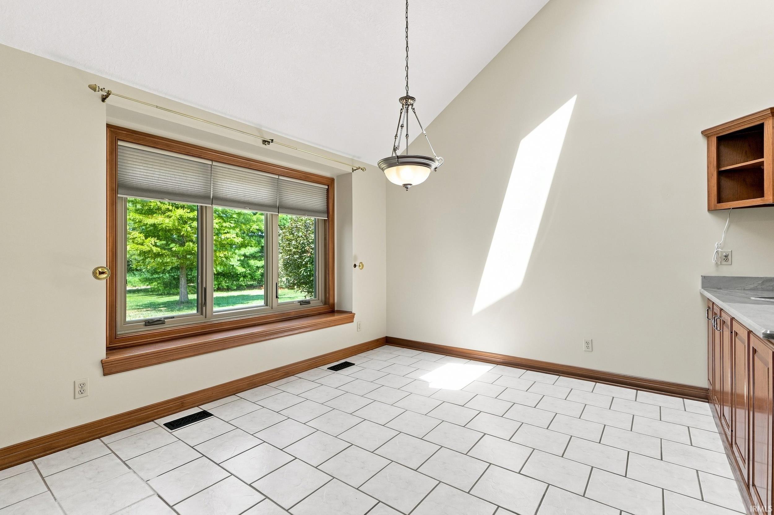 Vaulted ceiling, white tile flooring, wood trim, three-panel window, and an antique brass chandelier