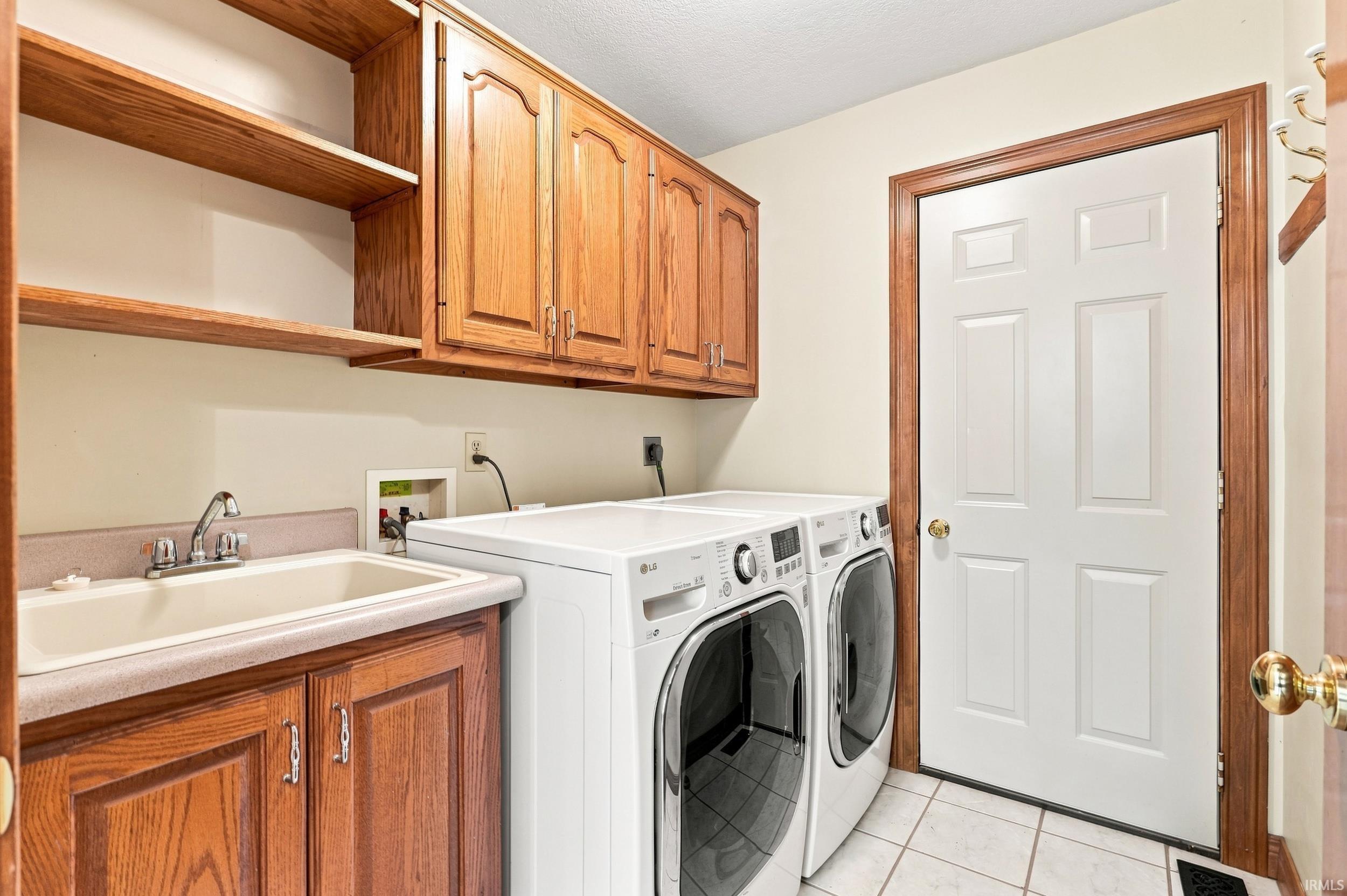 Dedicated laundry space featuring a utility sink, wood-finish cabinetry, open shelving, and tile flooring