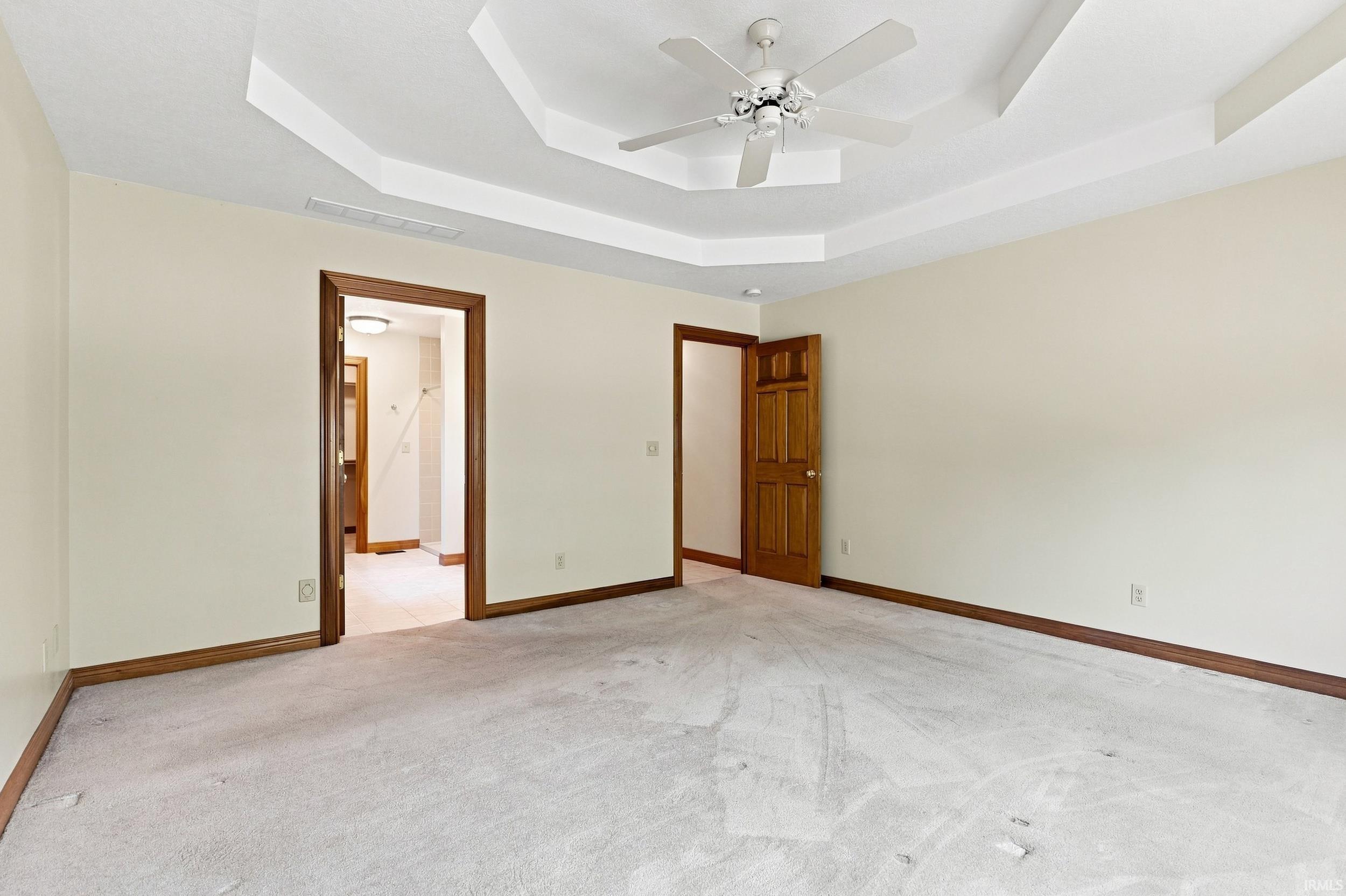 Spacious room featuring a tray ceiling, ceiling fan, carpet flooring, and wood trim