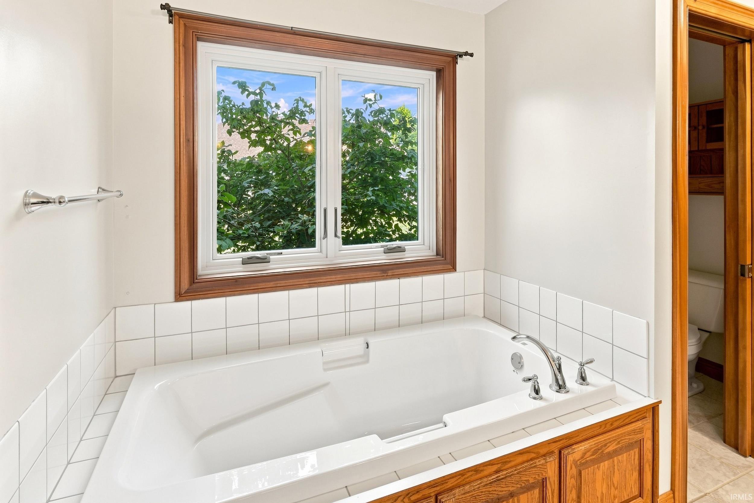 Built-in soaking tub with chrome fixtures, wood-finish surround, and white tile wainscoting