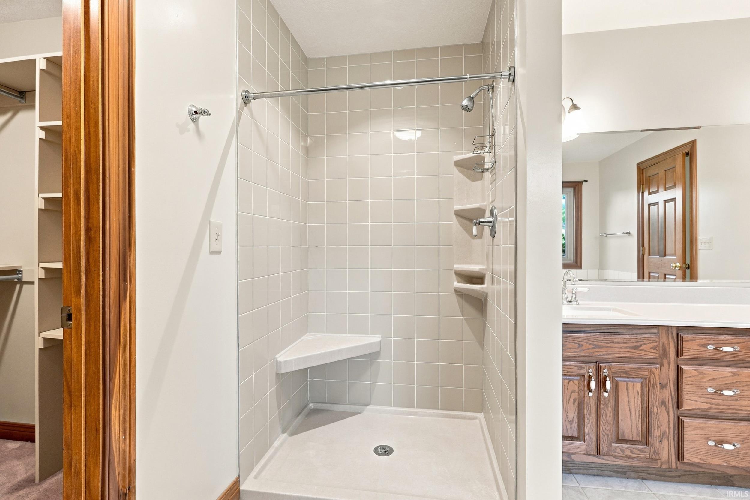 Modern walk-in shower featuring a frameless glass enclosure, white subway tile surround, integrated shelving niches, a rainfall showerhead with additional body jets, and a spacious base with integrated drain