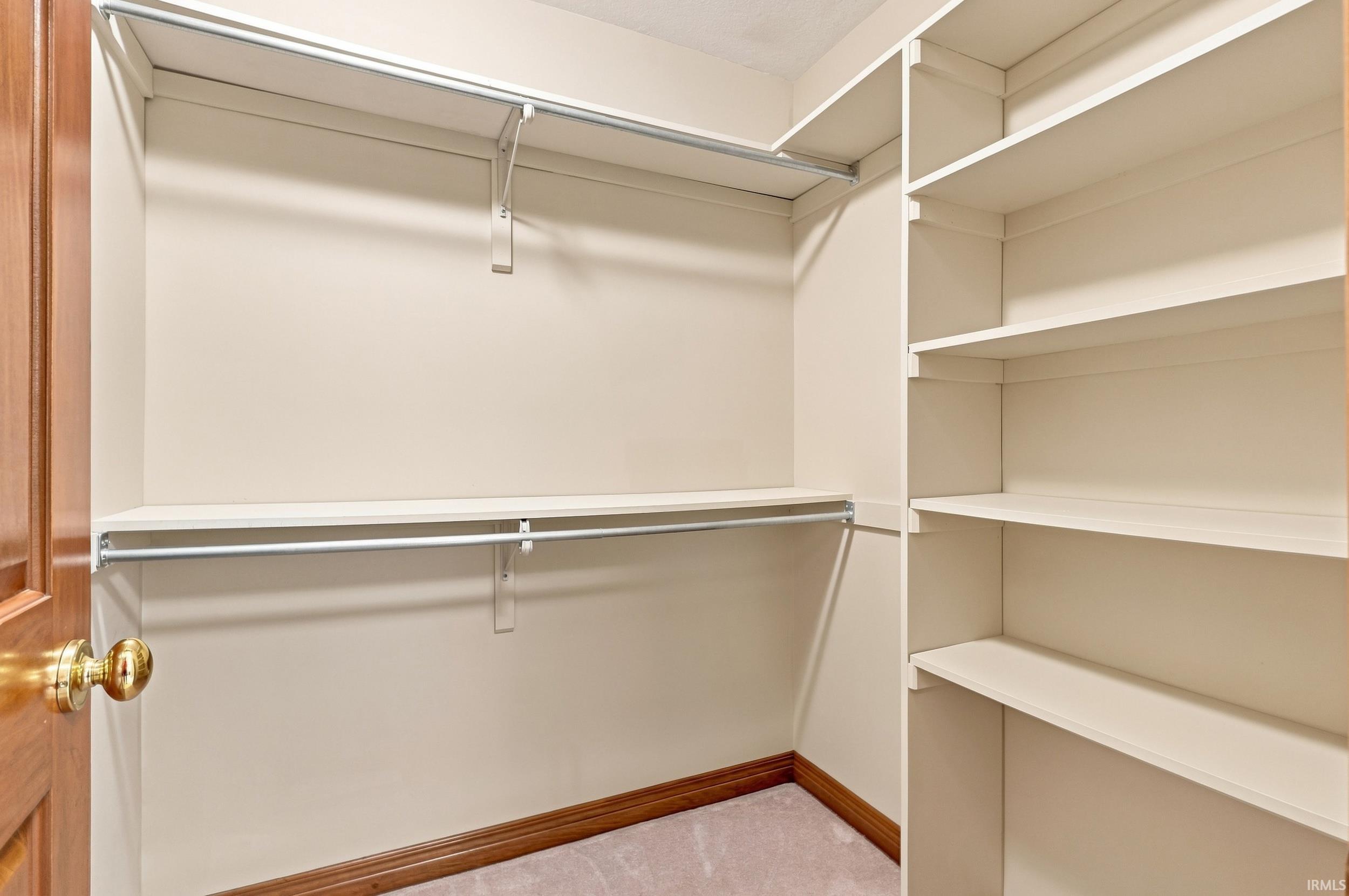 Walk-in closet featuring built-in shelving, two hanging rods, and wood-finish trim
